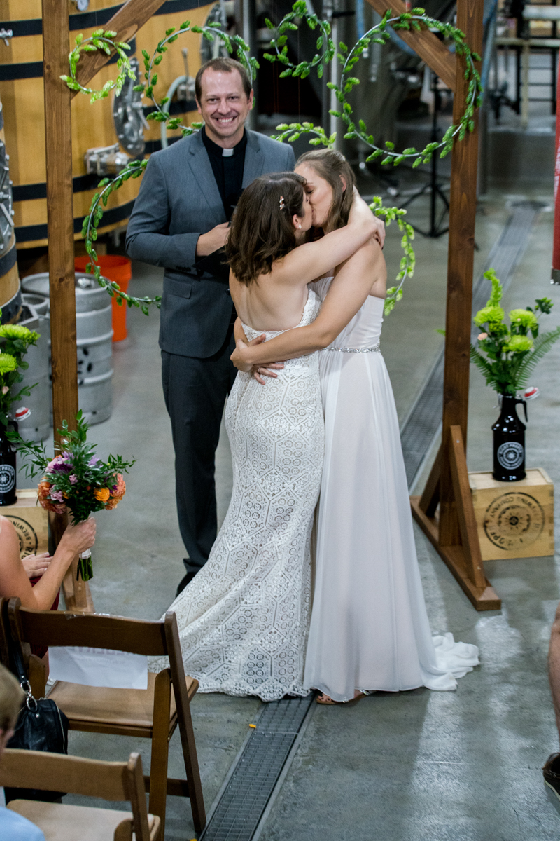 brides kiss at ceremony in front of altar with DIY hops wreaths at this DC brewery wedding Love Life Images