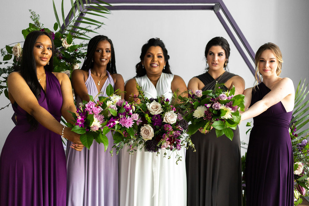 Henkaa fall wedding party dresses in purple and gray tones with bride in white and bridesmaids holding bouquets