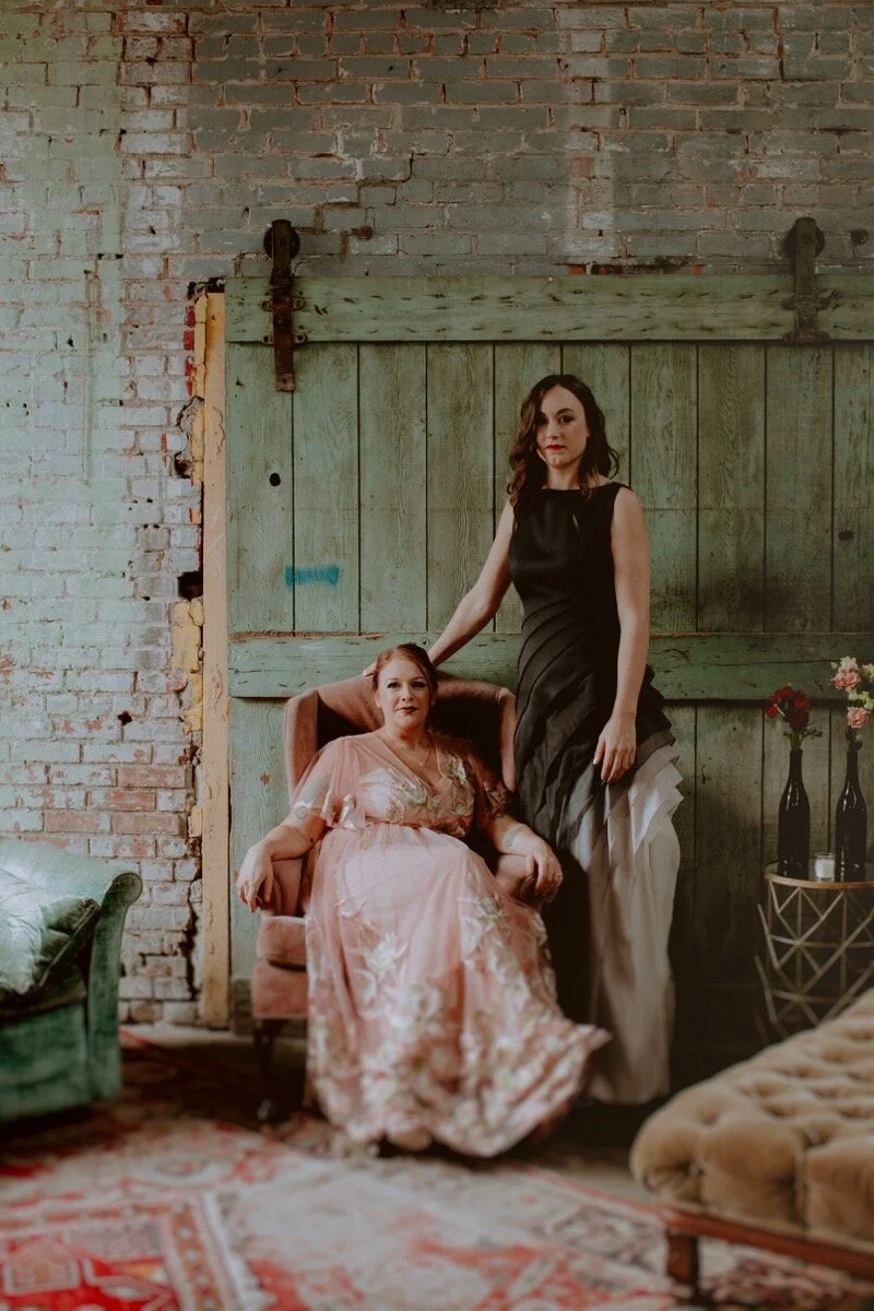 brides pose for portrait in vintage chairs at industrial wedding venue in Hudson New York Chellise Michael Photography