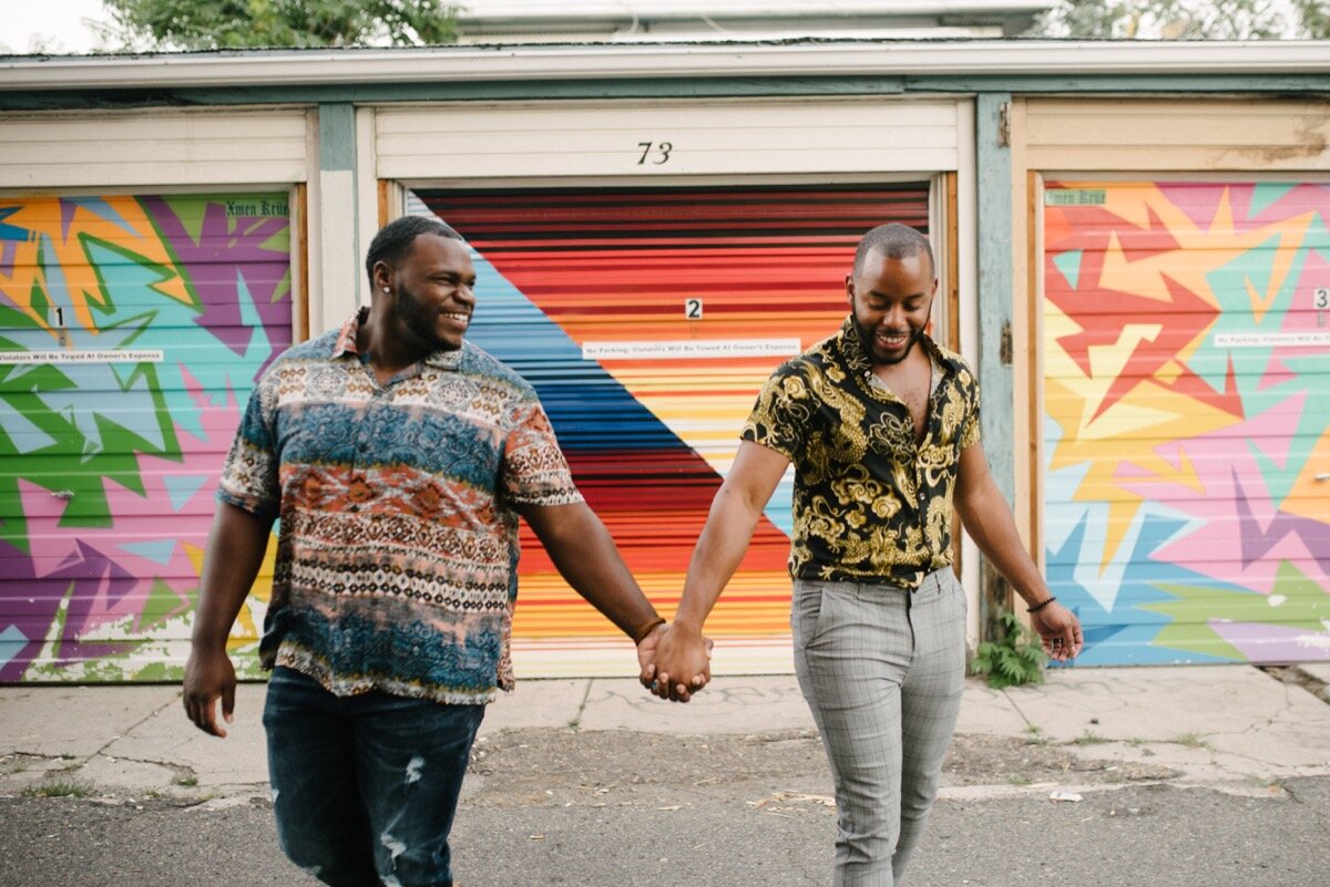 Chris and Nate hold hands by mural wall after surprise proposal at sugar bakeshop denver colorado Friends and Lovers Photography