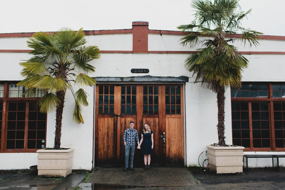 Couple stands in front of venue during wedding engagement photos in Seattle Fuck Yeah Weddings