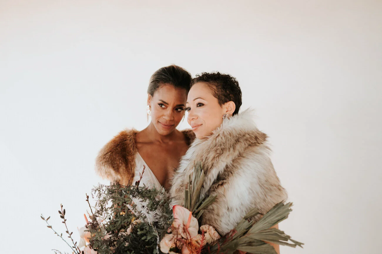 Newlywed brides embrace in front of blank wall Diana Ascarrunz Palm Springs Wedding Photographer