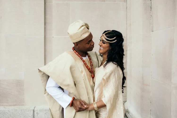 Multicultural newlyweds embrace in front of stone wall Couple holding hands during wedding ceremony as family wipes away tears Richmond Virginia Betty Clicker Photography