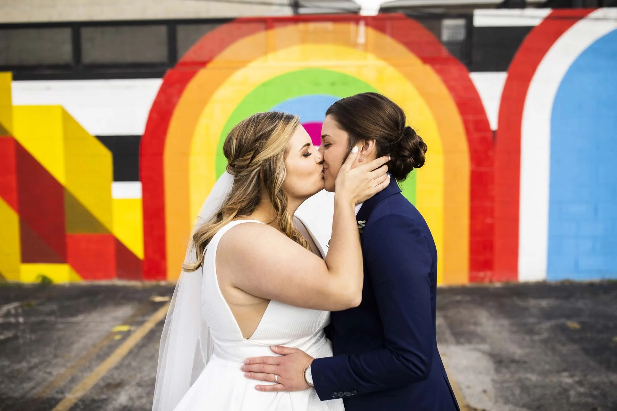LGBTQ couple in wedding dress and suit kiss in front of rainbow mural in Ohio Amy Ann Photography