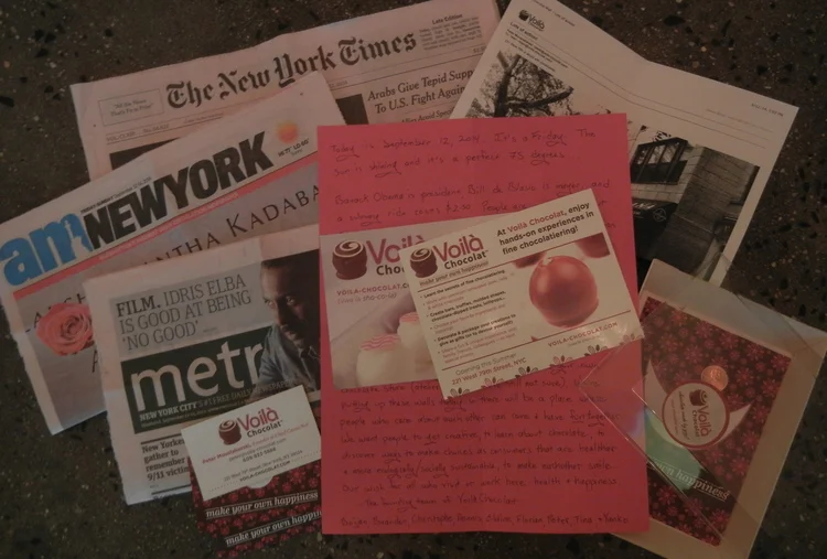 In our time capsule: today's papers, some of our business cards, a 2014 penny, an email with an update about the construction of the store, postcards, and a note to the future from our team (text intentionally obscured here). "Our wish for all who visit or work here: health & happiness. -- The founding team of Voilà Chocolat"