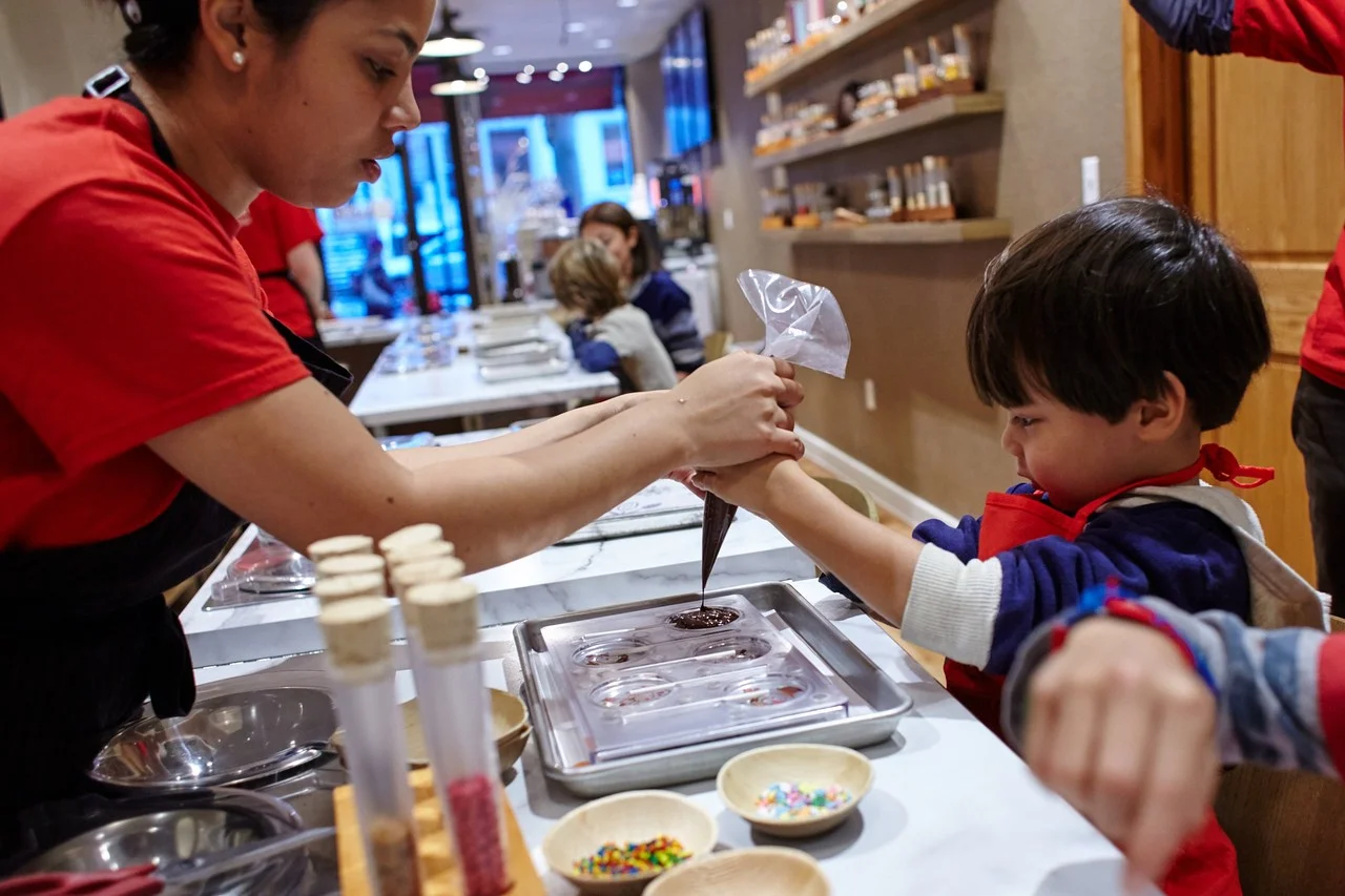 Life is sweet indeed at Voilà Chocolat: Anna Urena helps Bailey Chou Almeraz make lollipops. STEVE REMICH FOR THE WALL STREET JOURNAL