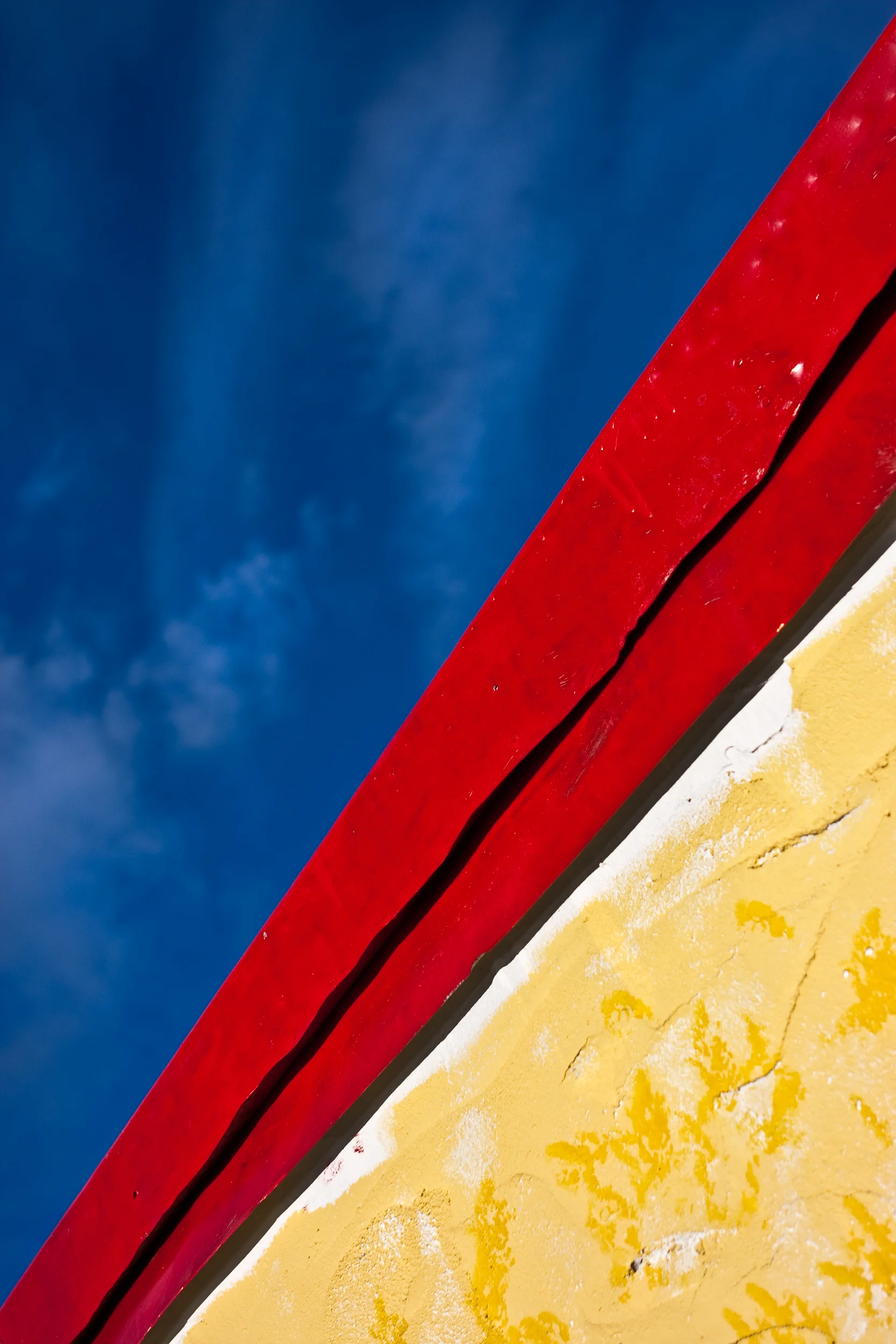Detail abstract image of a red roof with yellow walls against a cloudy blue sky.