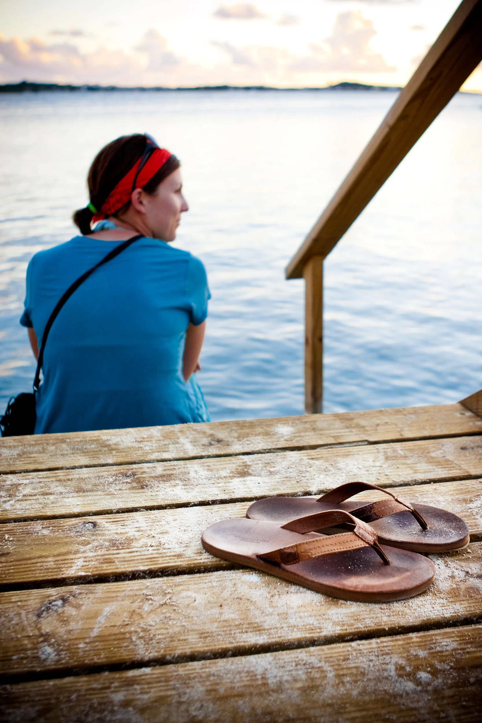 Woman admires a sunset view over blue water during a sailing vacation with her flip flops in the foreground.