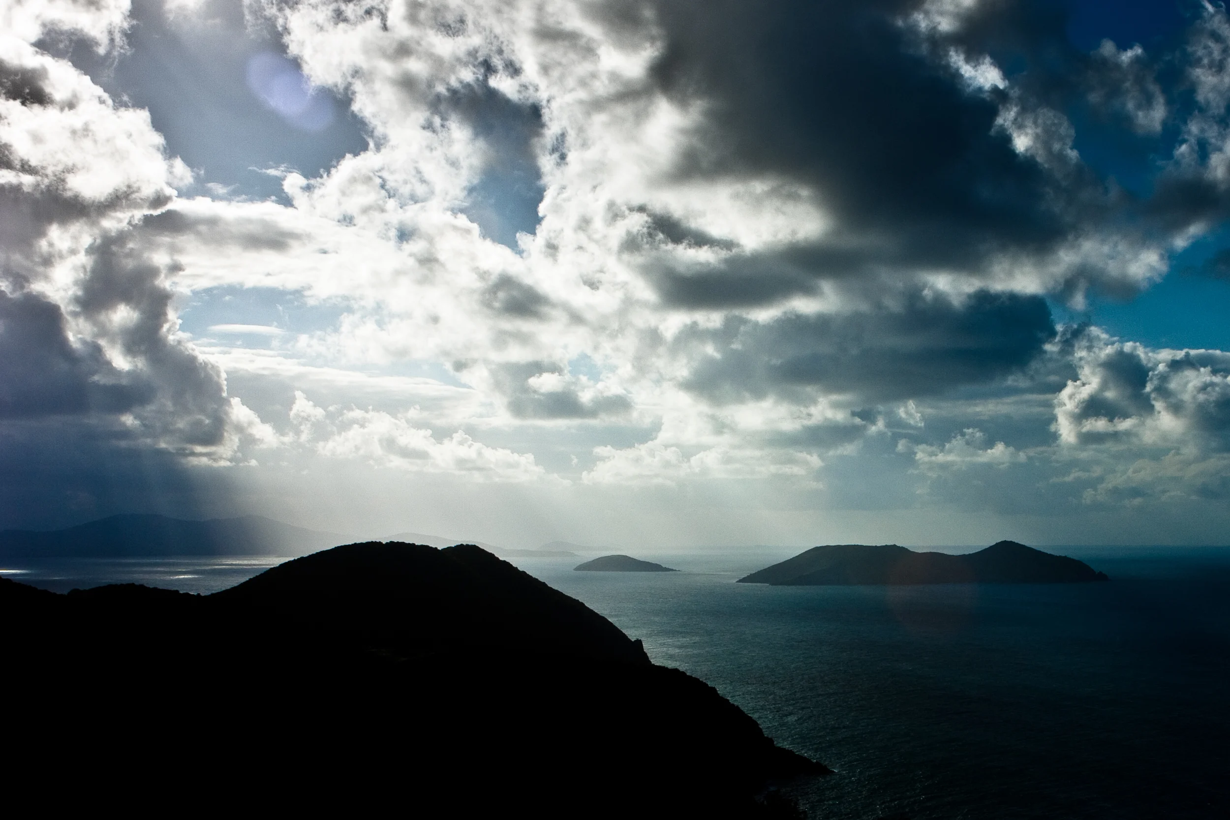 Sunlight rays stream through storm clouds over a chain of islands and silhouettes.
