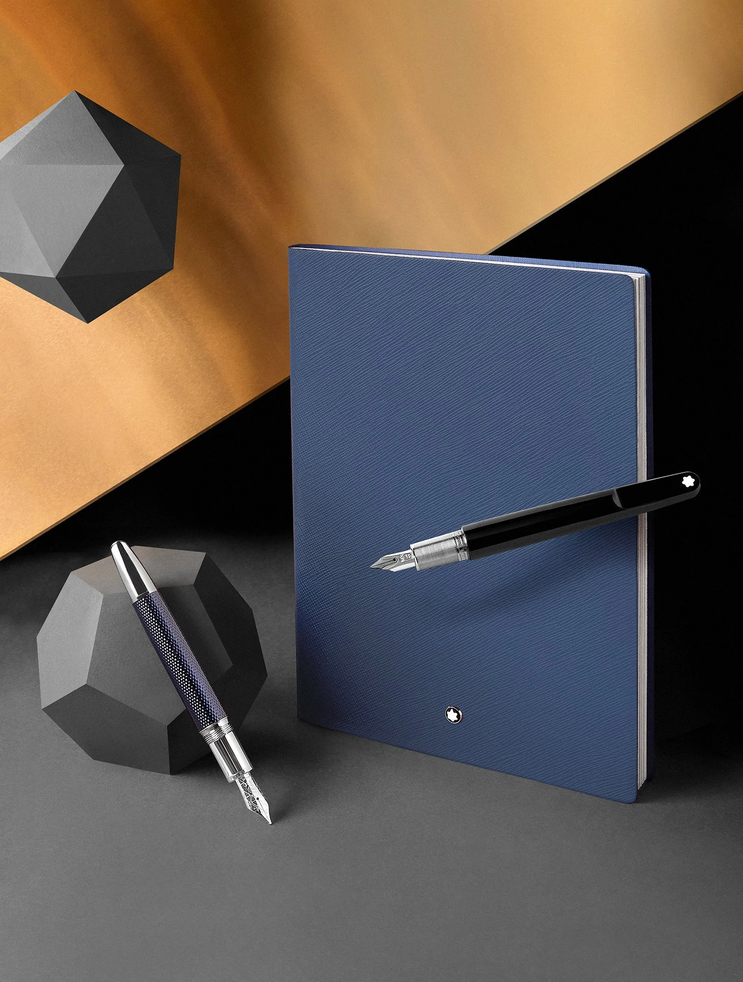  Montblanc notebook and pens shot by London based still life photographer Josh Caudwell. Creative still life photography of tabletop scene with luxury pens and notebook with floating geometric shapes. 