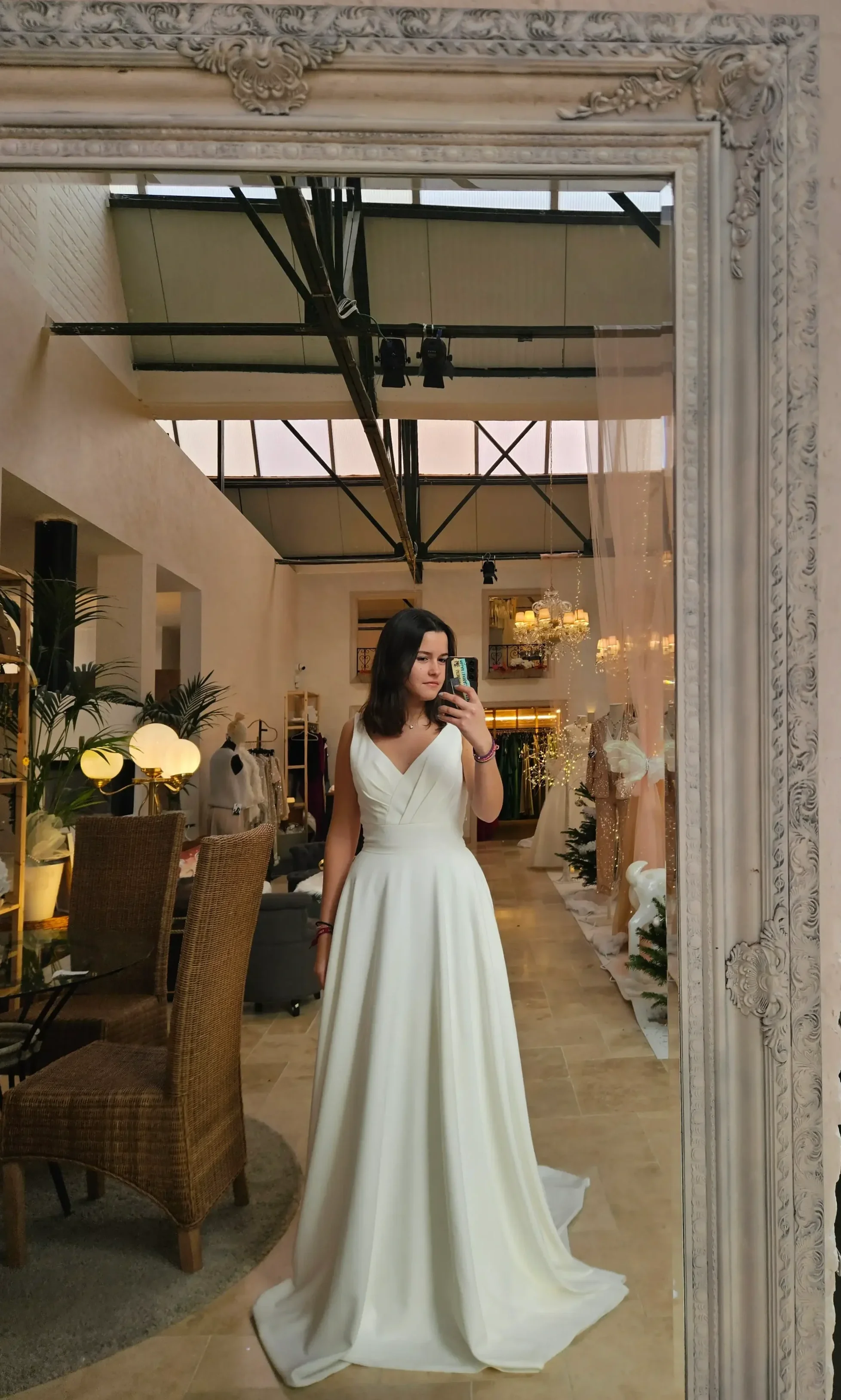 Fille prenant une selfie dans un miroir, portant une robe de mariage blanche dans un magasin de vêtements ou un studio de mariage décoré pour Noël.