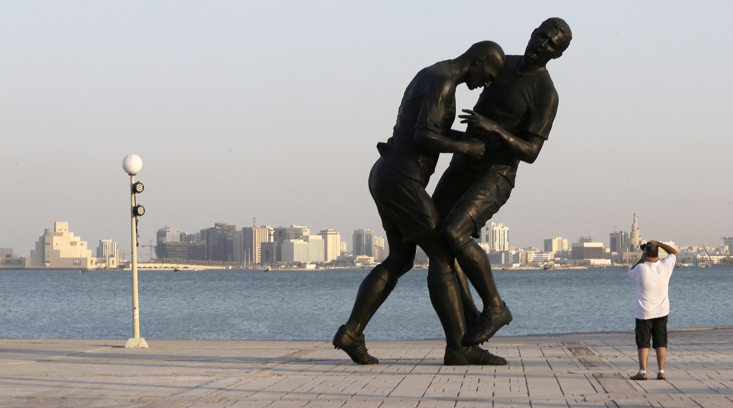 A man takes pictures of a bronze sculpture titled 'Coup de Tete' by Algerian-born French artist Adel Abdessemed during its installation on the Corniche in Doha October 7, 2013. The sculpture, which was bought by the Qatar Museums Authority, was removed on October 28, 2013 after generating criticism from religious conservatives, according to local media. The art work portrays French footballer Zinedine Zidane headbutting Italian player Marco Materazzi during the 2006 World Cup. Image supplied by Action Images
