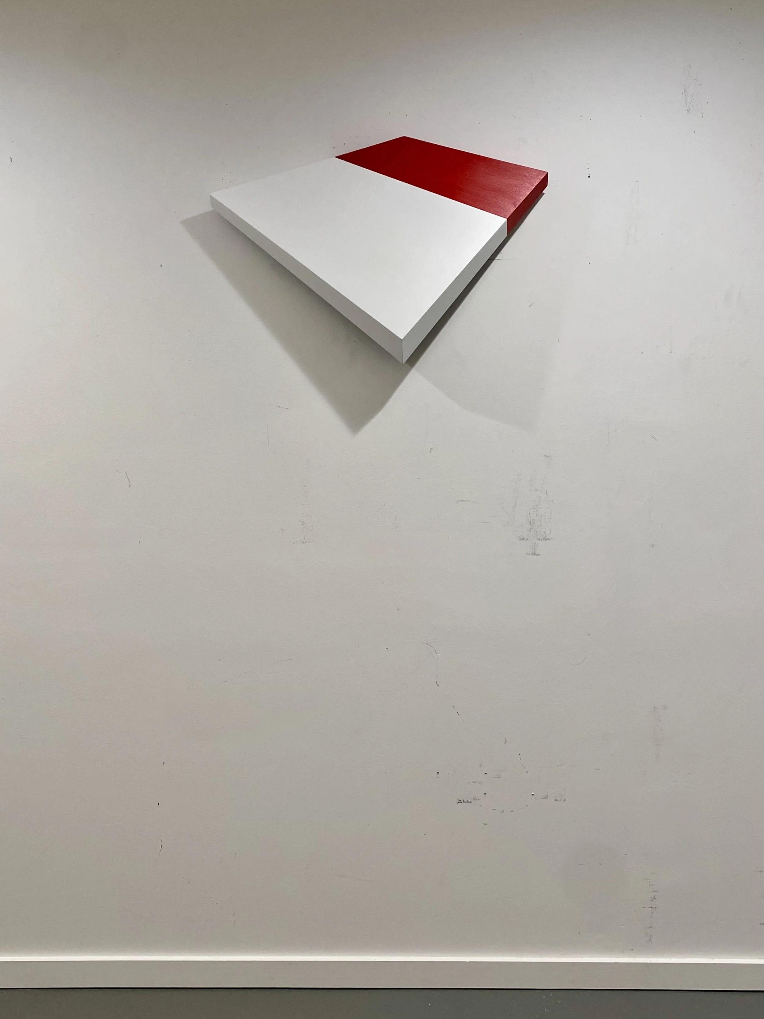 (Red–White) Tilted Plane , 2026. Enamel, hand-cut and shaped wood relief. 15 × 23 × 5 inches. The foreshortened effect is exaggerated when seen head on. The form physically tapers from thick to thin along all four sides
