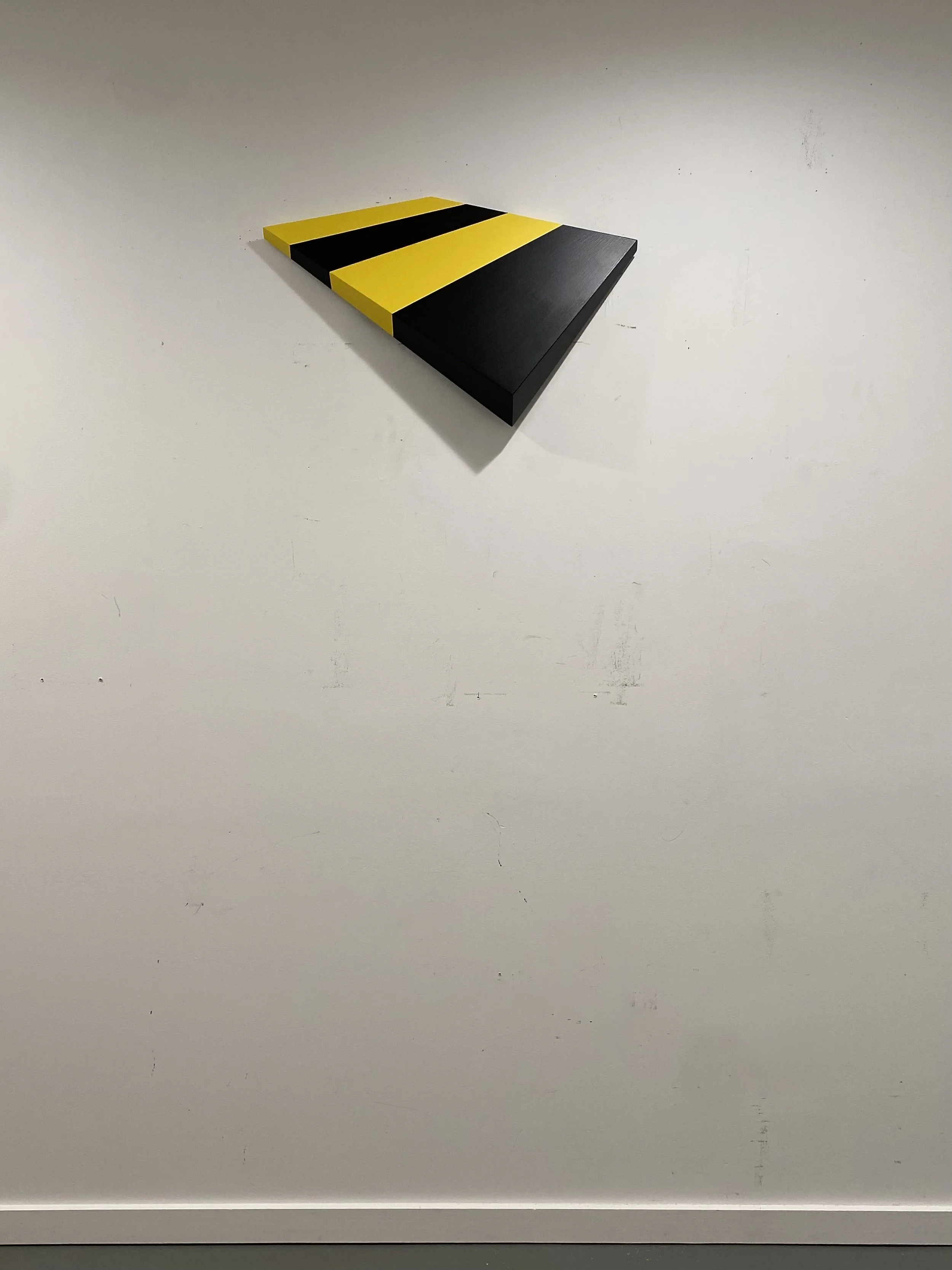 (Yellow-Black) Tilted Plane , 2026. Enamel, acrylic, hand-cut and shaped wood relief. 14 × 23 × 3 inches. The foreshortened effect is exaggerated when seen head on. The form physically tapers from thick to thin along all four sides