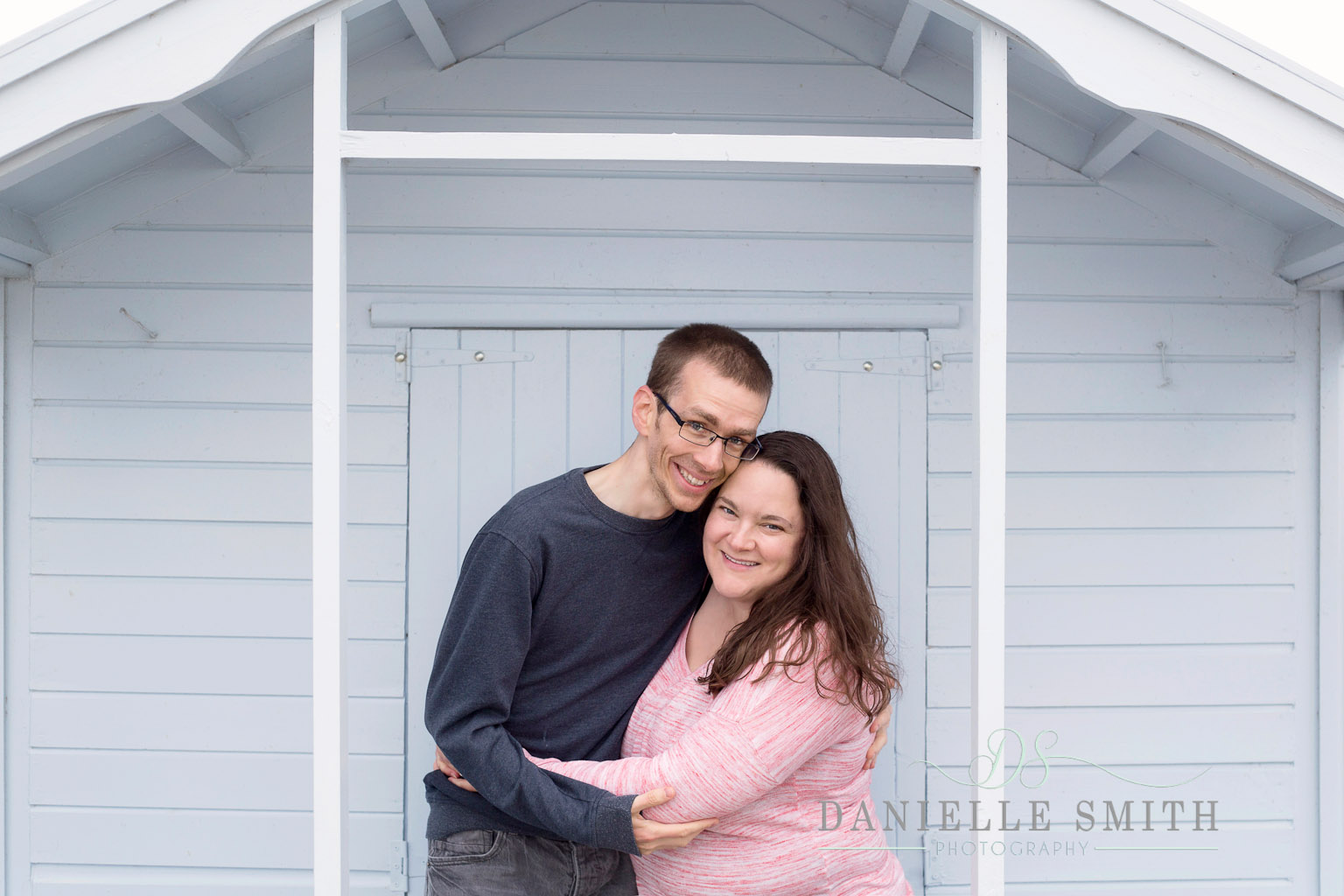 couple in front of blue beach hut - seaside engagement photo shoot