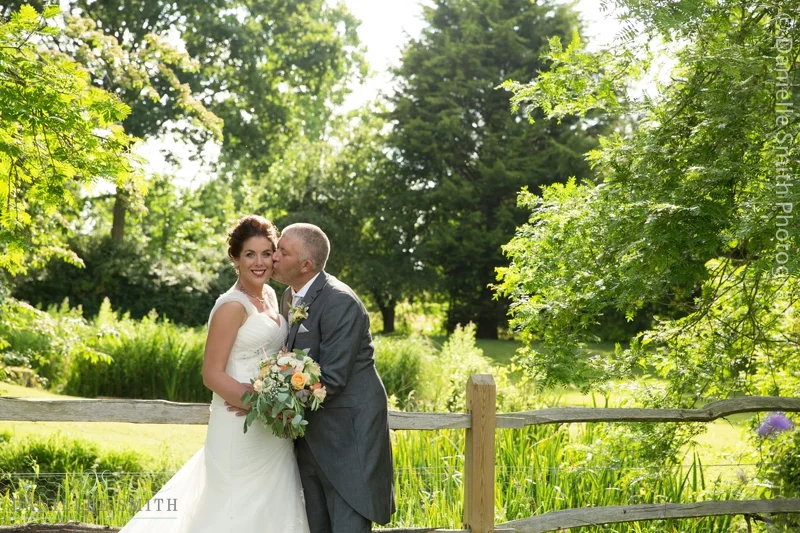 groom kissing his wife on cheek in gardens - houchins wedding photography