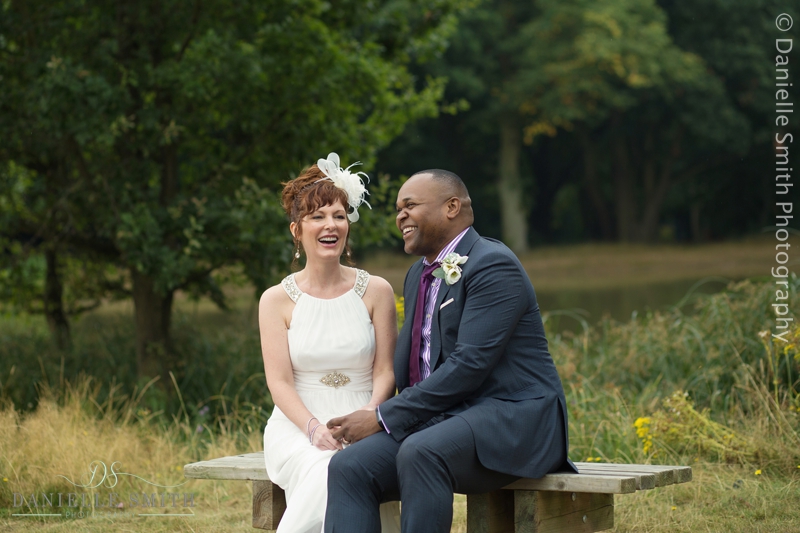 bride and groom sitting on bench in front of lake
