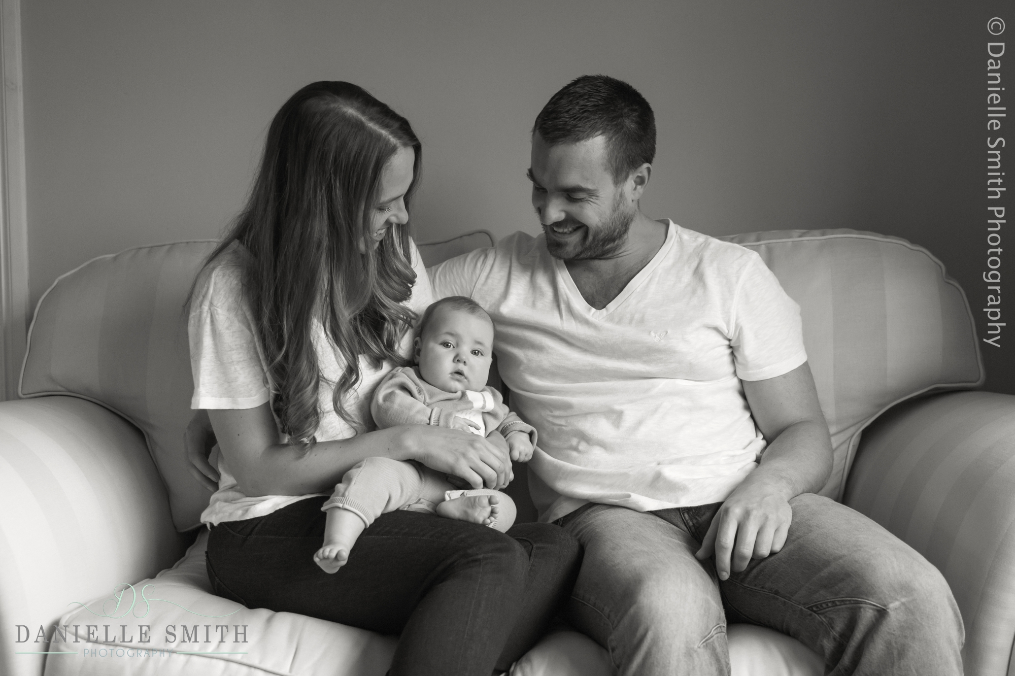 mum and dad sitting on sofa with baby - baby photo shoot at home