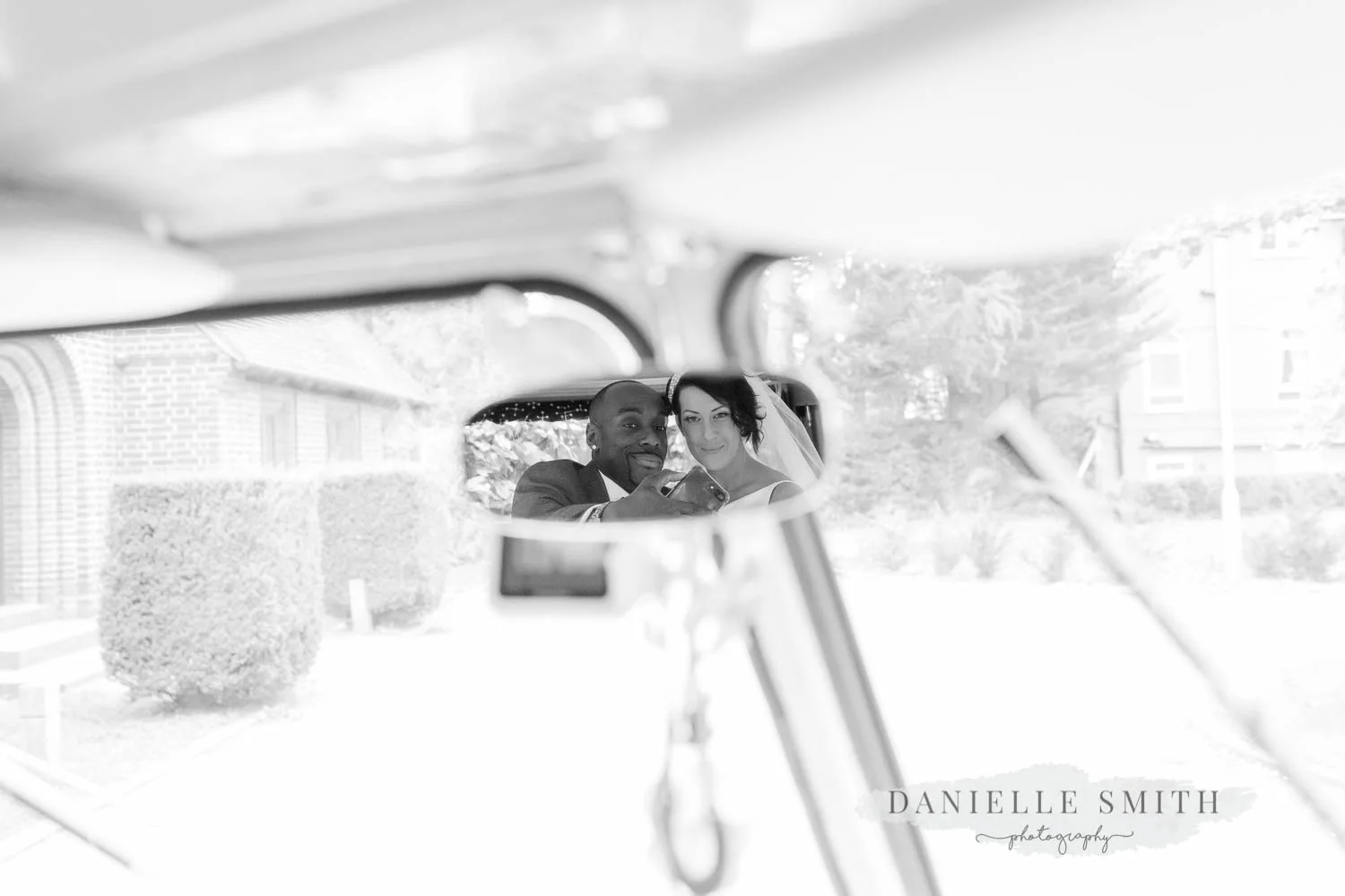 bride and groom having selfie in car mirror