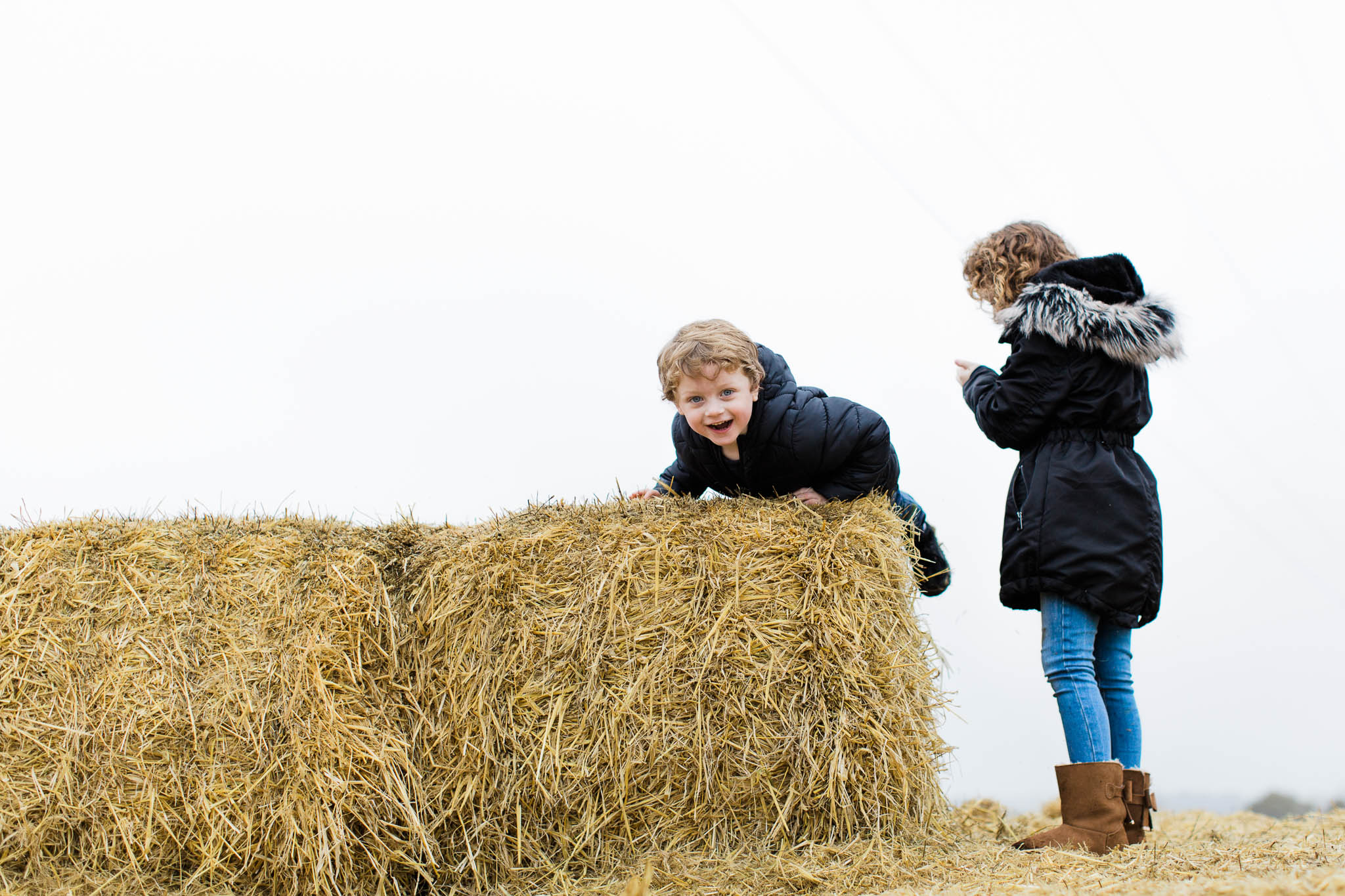brother and sister climbing on hay stacks