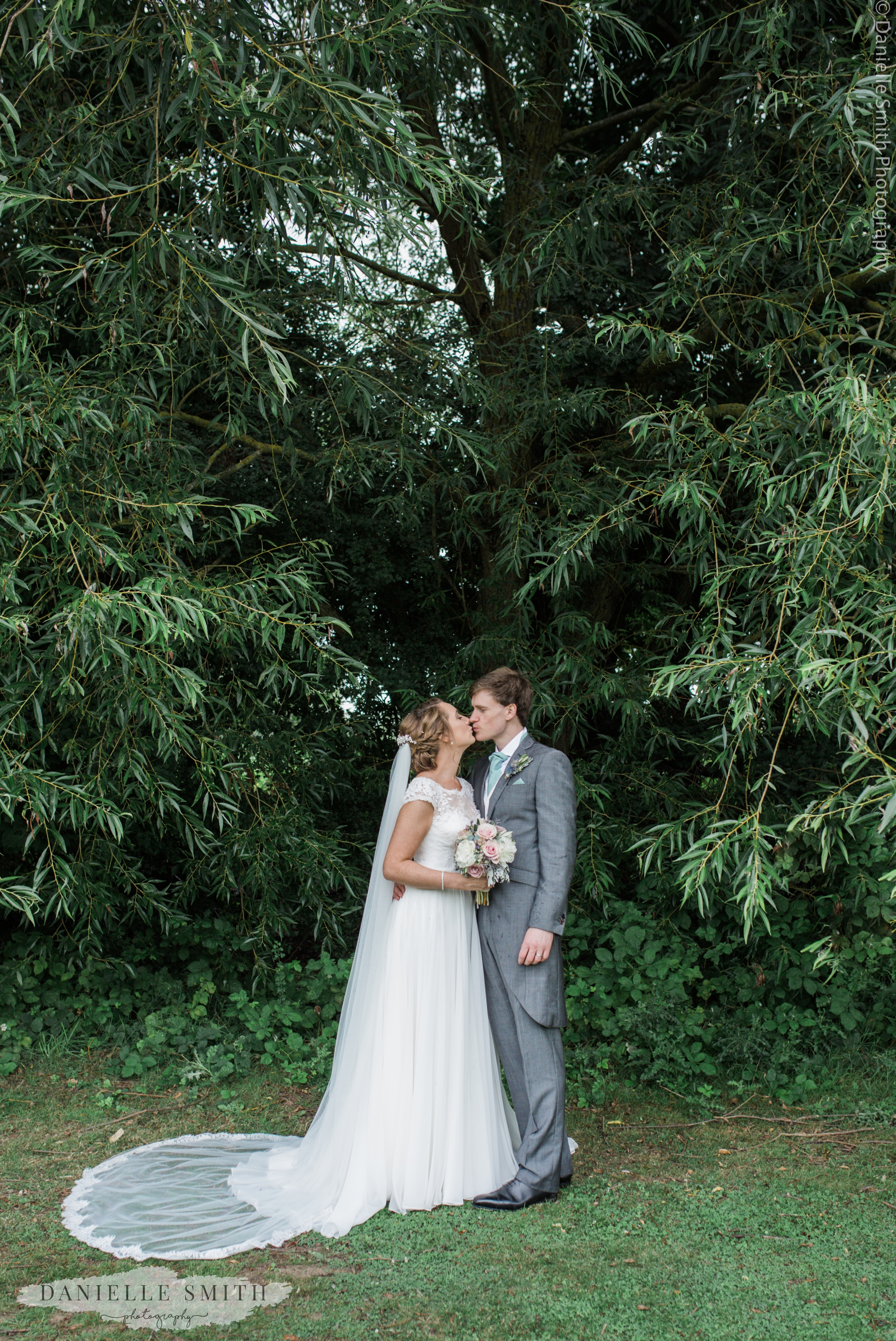 bride and groom kiss under tree