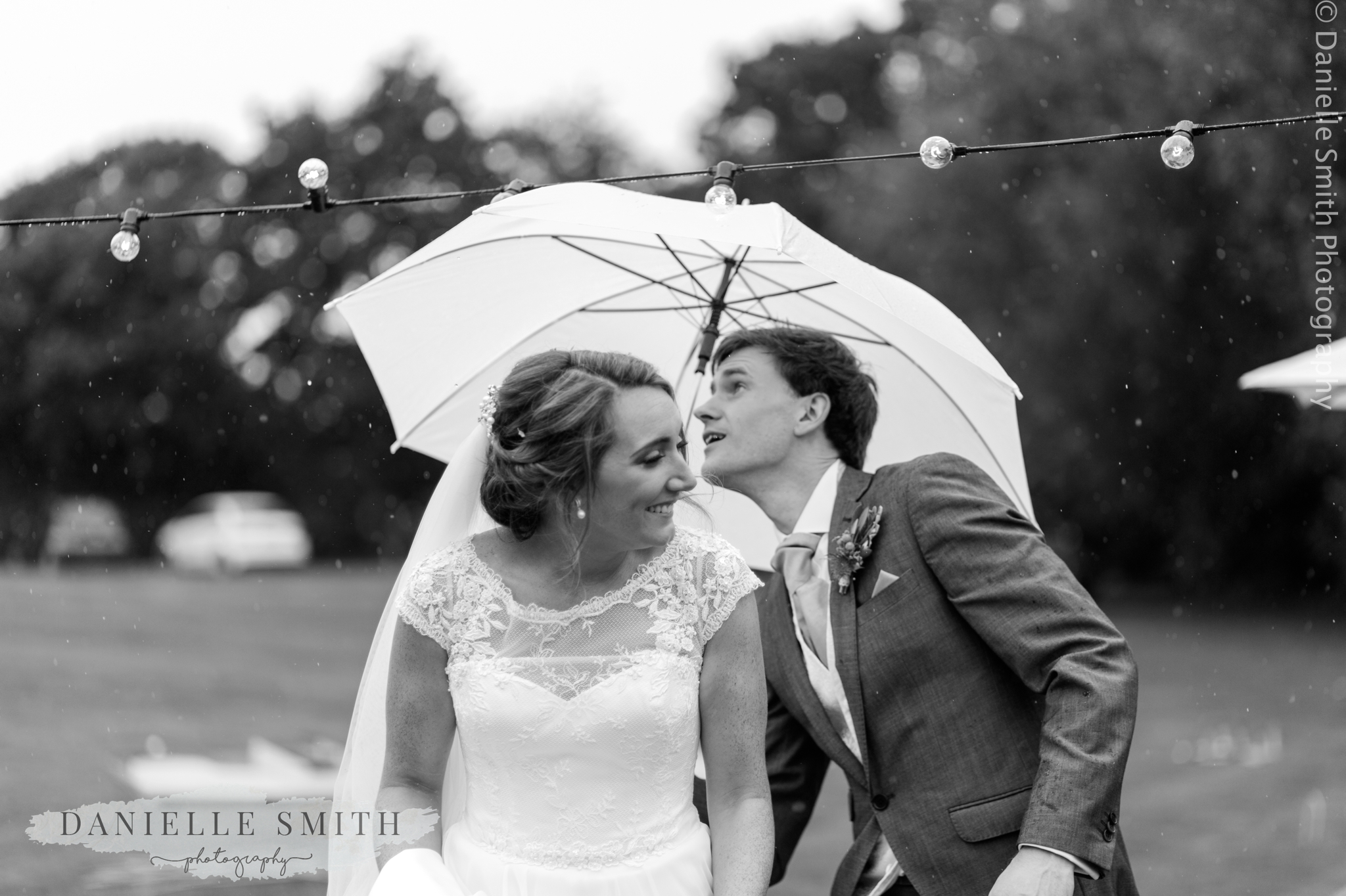 bride and groom ducking under lights with umbrella
