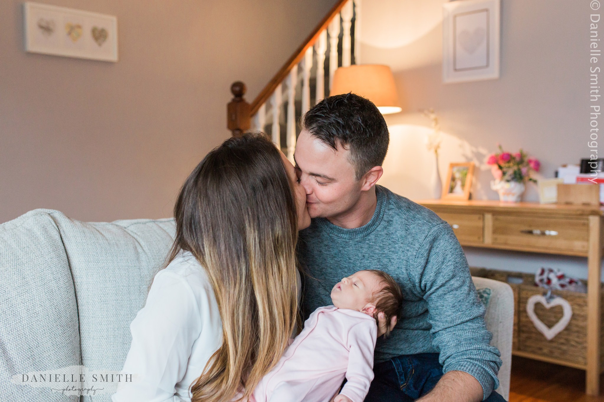 mum and dad kissing holding baby girl