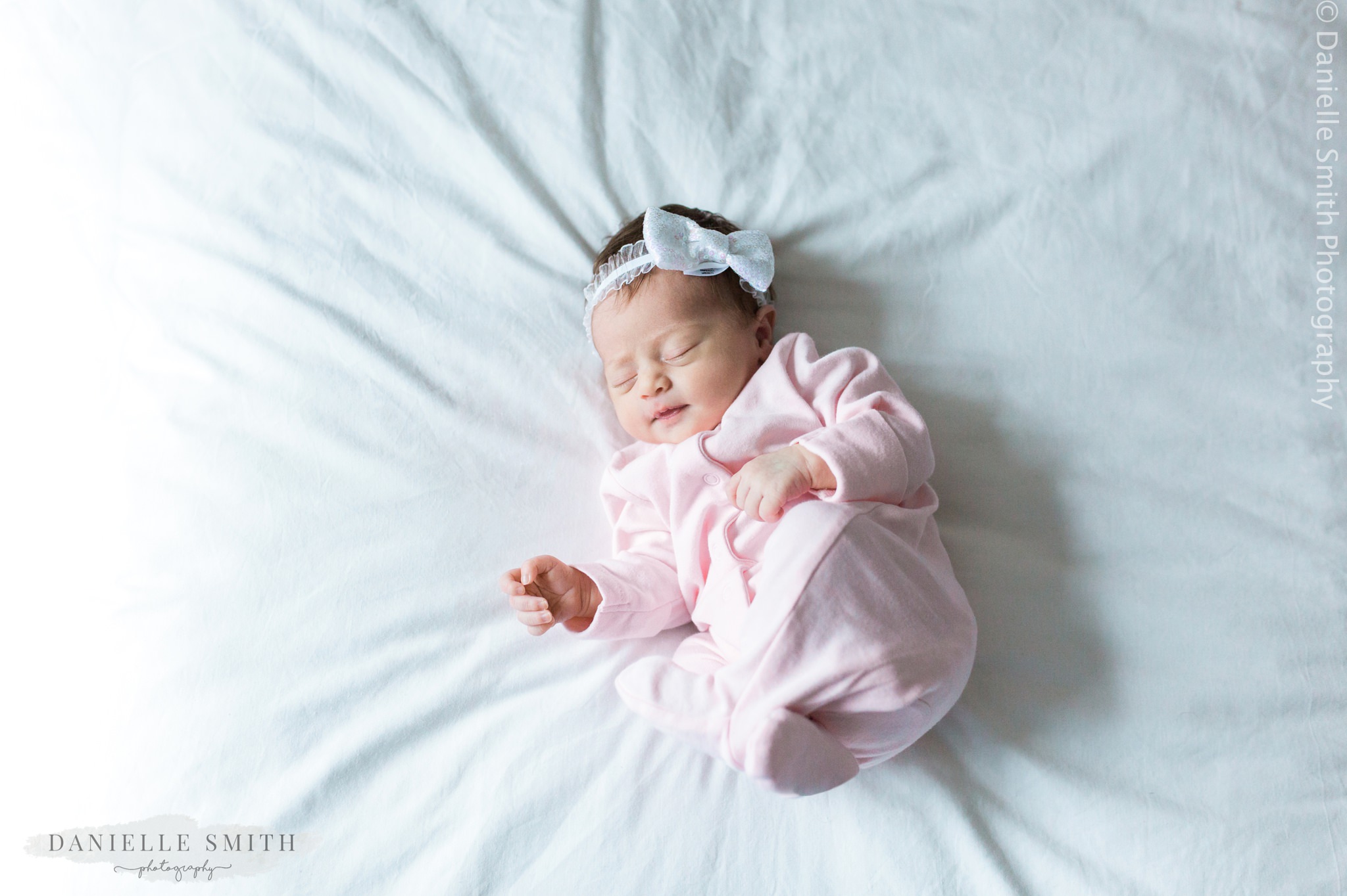 newborn baby girl lying on bed in pink baby grow