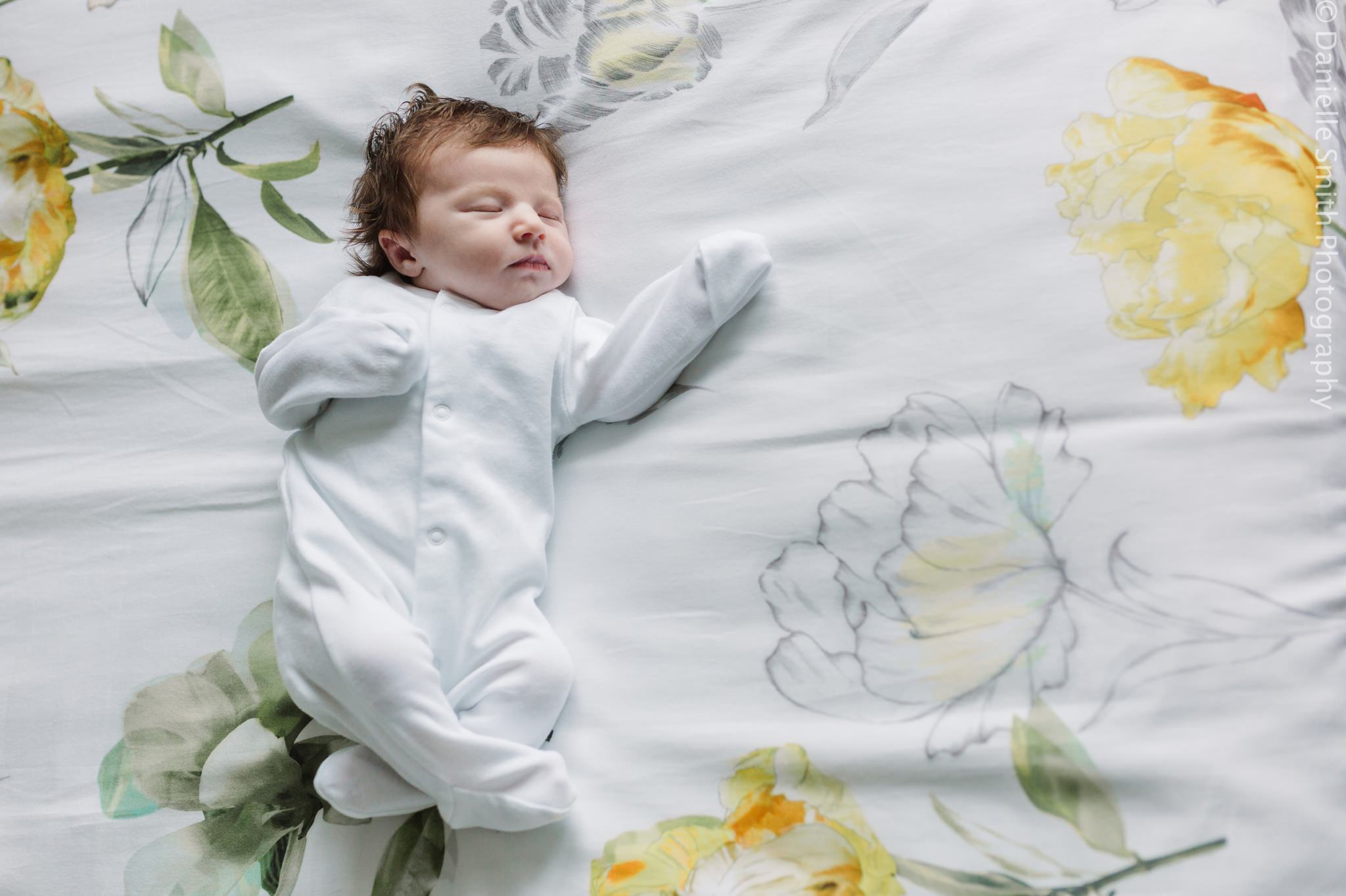 newborn baby in baby grow on bed