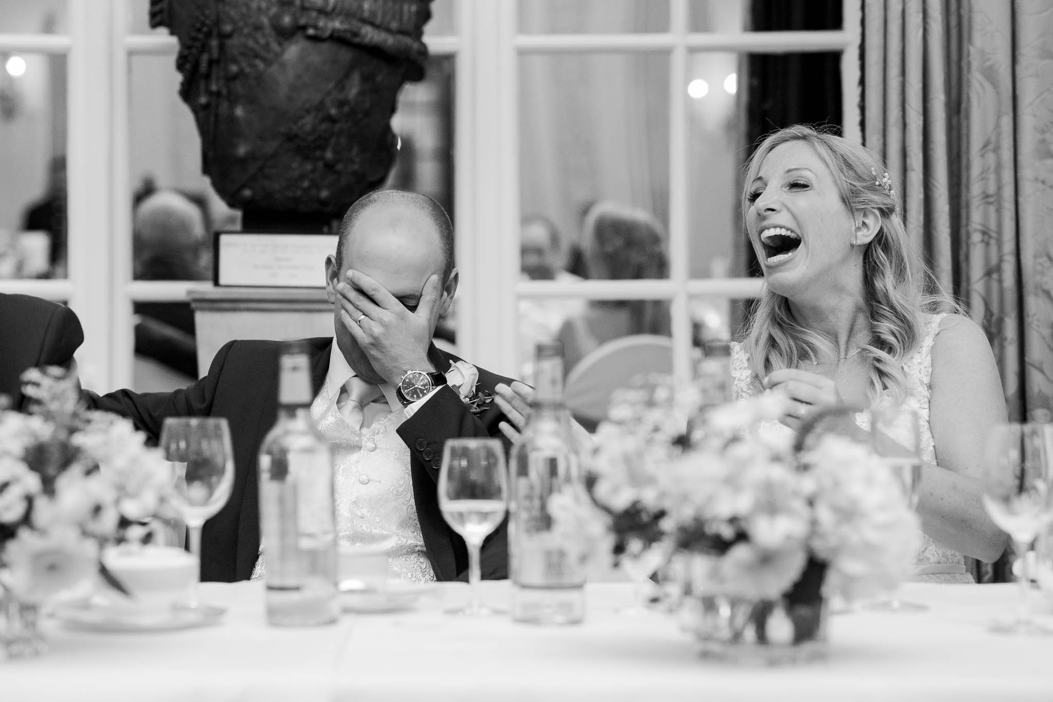 groom covering face and bride laughing during best man speech