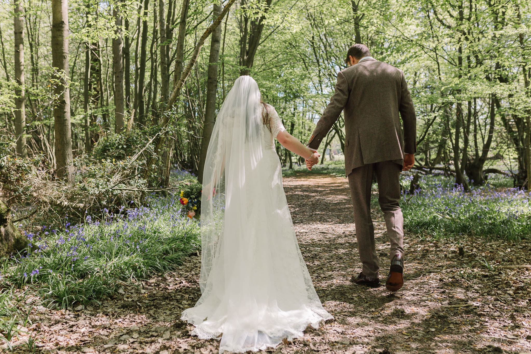 bride and groom walking through bluebell woods