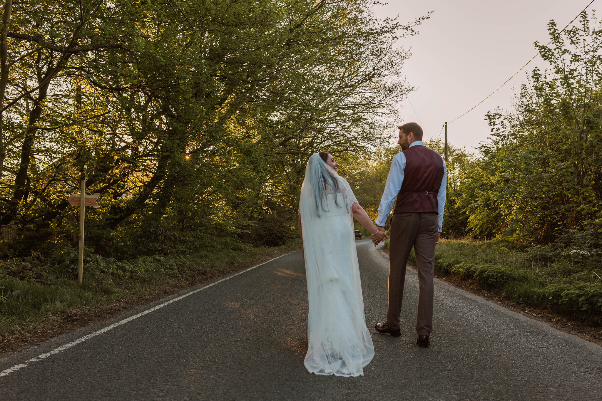 bride and groom walking down road at sunset
