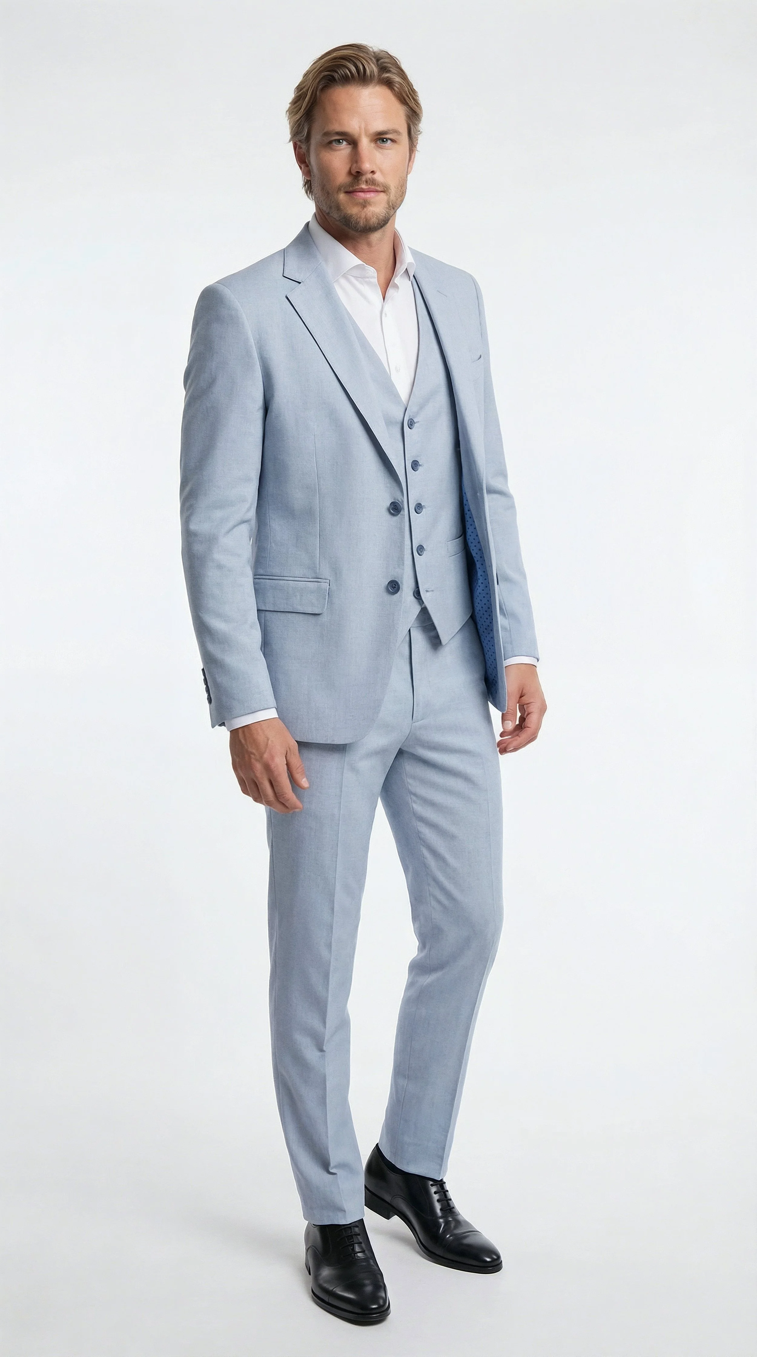 A man in a light blue suit with a white shirt and black shoes standing against a plain white background.