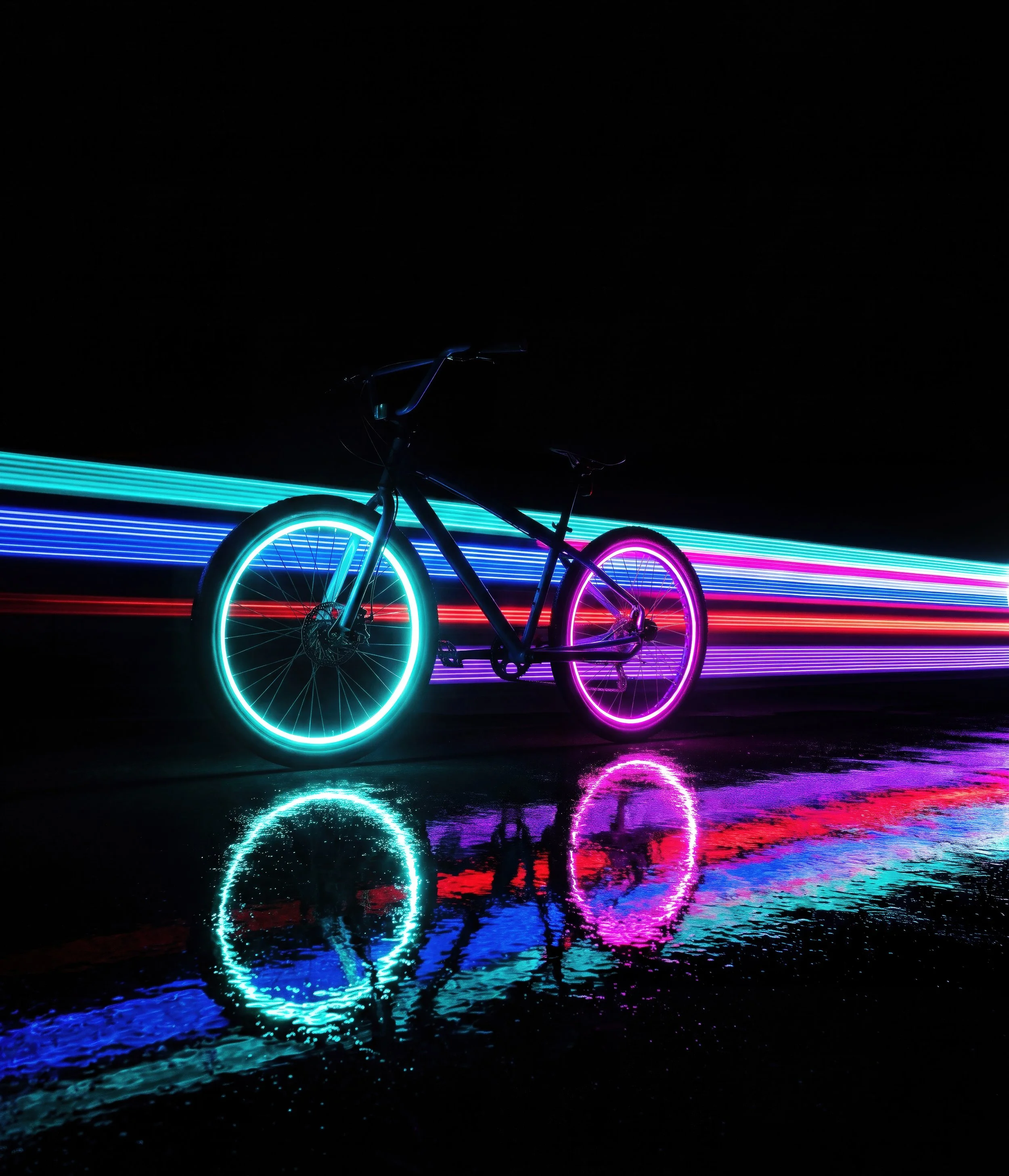 A bicycle with glowing neon tires and frame is reflected in a body of water with colorful light streaks in the background at night.