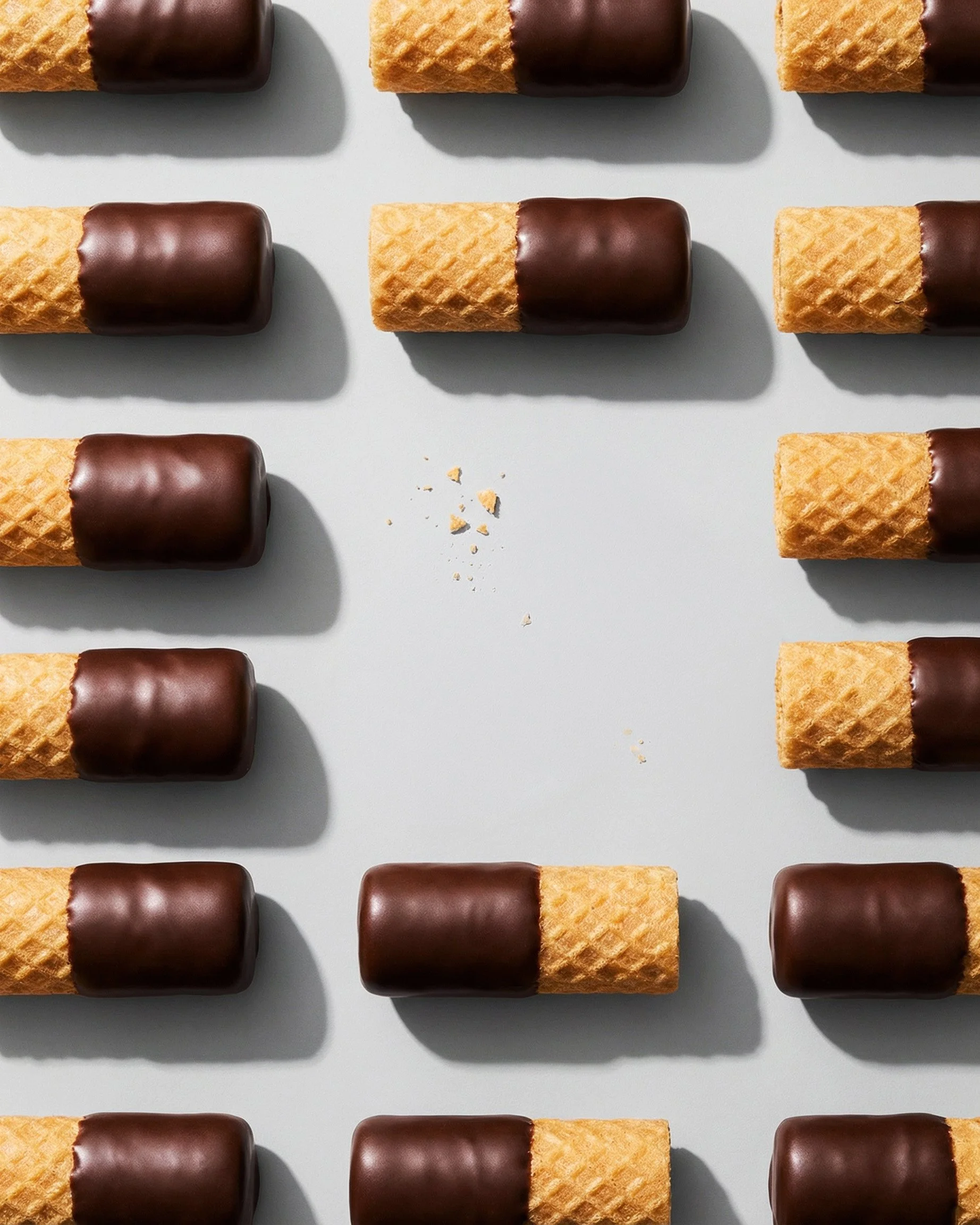 Rows of chocolate-dipped waffle cones arranged neatly on a light gray background, with a few crumbs in the center.