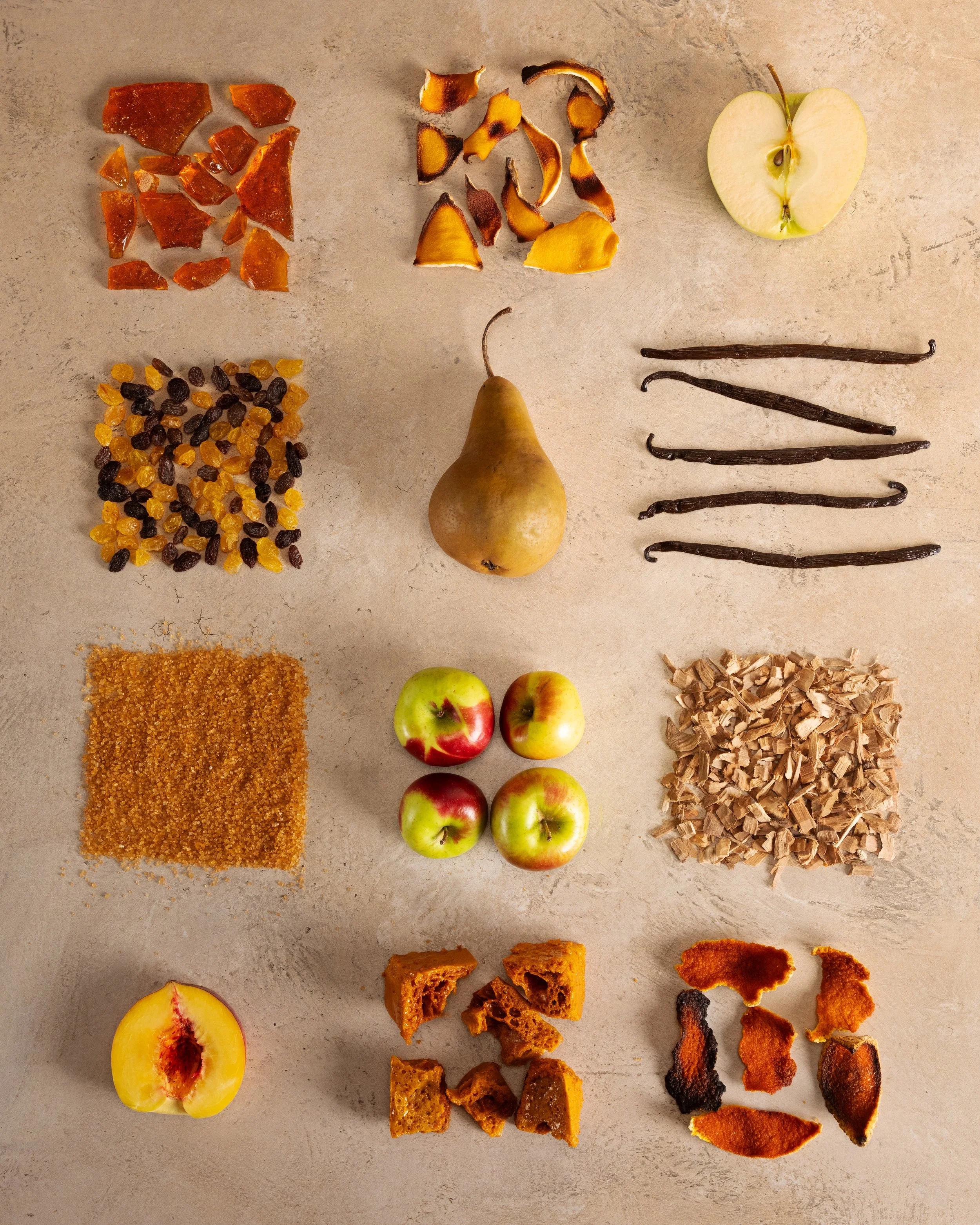 Arrangement of various dried fruits, spices, and fresh fruits on a neutral surface, including apple slices, pears, apples, dried oranges, ginger, vanilla beans, raisins, chopped dried apricots, dried apple rings, and dried peaches.