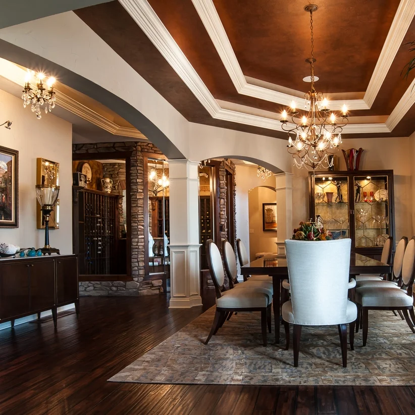 Luxury formal dining room with coffered ceiling, elegant chandeliers, dark hardwood floors, and custom architectural archways.