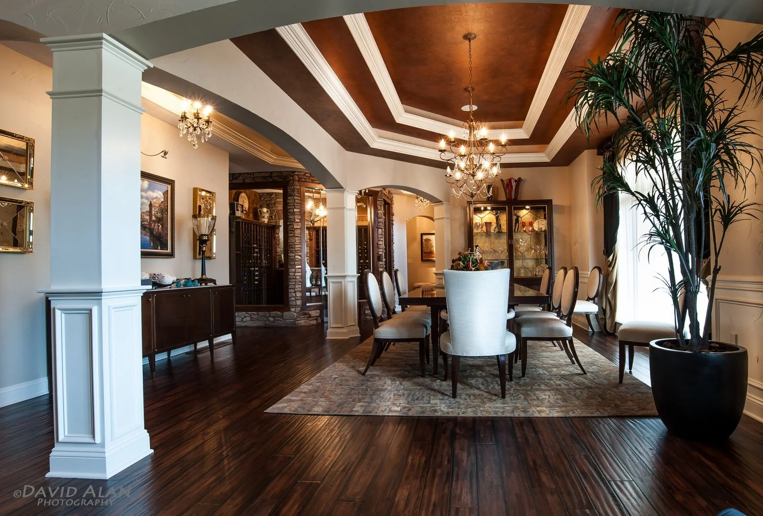 Luxury custom home dining room with tray ceiling, chandeliers, arched openings, and hardwood floors in Northeast Ohio