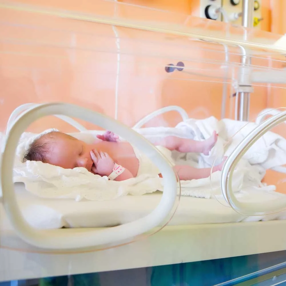 nicu baby unswaddled in isolette with hospital bracelet, iv pump