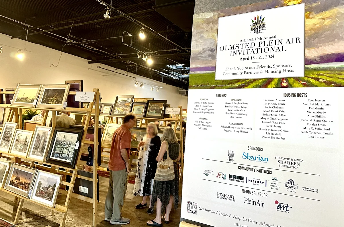 An art gallery with several framed paintings displayed on wooden easels and walls, and three people talking in the foreground. A large event poster for the Olmsted Plein Air Invitational 2024 is visible on the right.