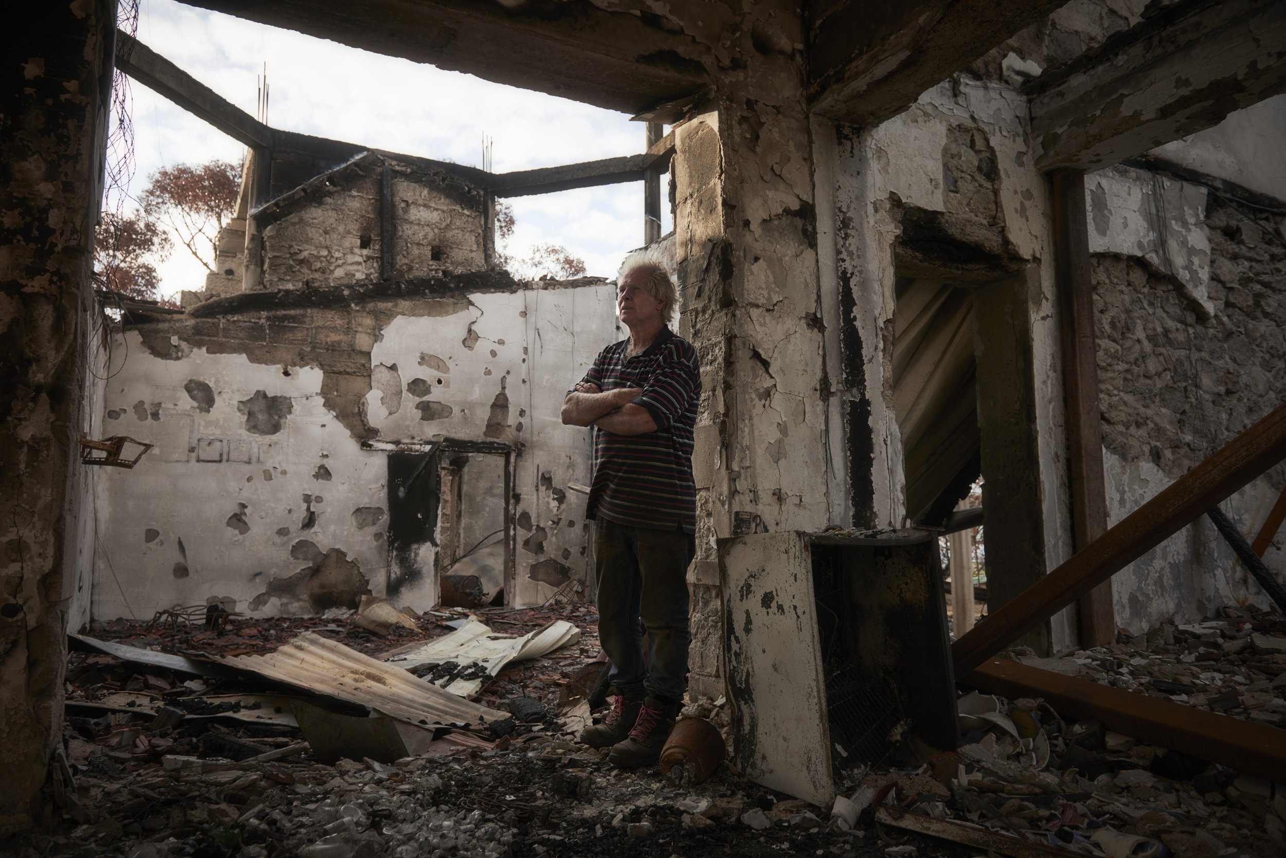  Paul Stanton surveys his home in March 2020 as his new reality still is difficult to accept, months after the fires destroyed his home. “I started building it 46 years ago; it was nearly finished. I had even kept some of the walls from the original 