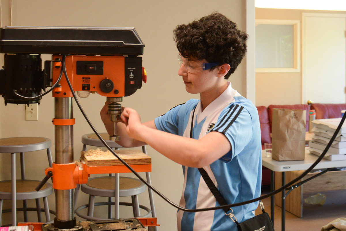  Anabel sets up the drill press to make a perfectly straight hole for their steering device. 