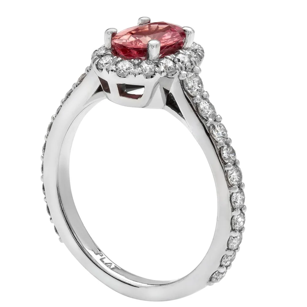 1.15 carat Oval Cut Padparadscha Sapphire Ring. 0.88 carats of round brilliant cut Diamonds surround the center stone. Set in platinum.