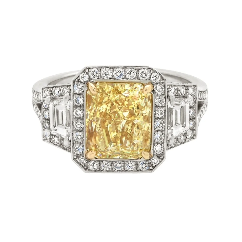 3.05 carat Radiant Cut Fancy Yellow Diamond Halo 3 stone Ring. Trapezoid Cut Diamond side stones and 0.82 carats of Round Brilliant Cut Diamonds. Set in 18k yellow gold and platinum.