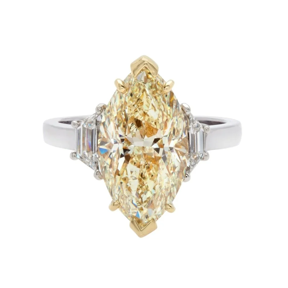 6.01 carat Marquise Cut Light Yellow Diamond  3 stone Ring. 0.66 carats of Trapezoid Cut Diamonds surround the center stone. 6.67 carat total weight. Set in 18k yellow gold and platinum.