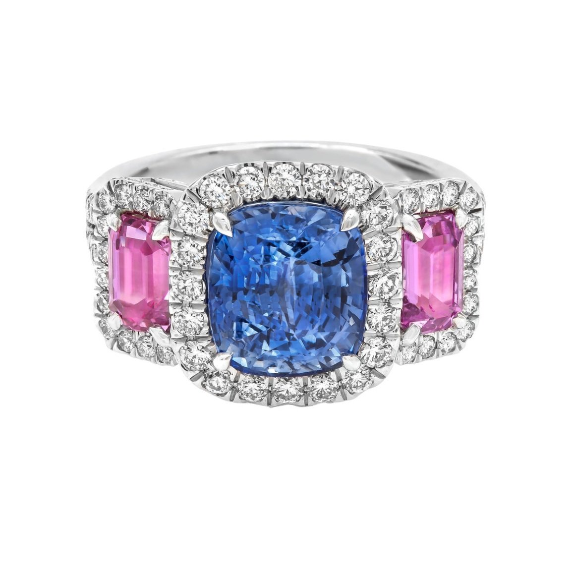 4.33 carat Cushion Cut 3 stone halo Sapphire Ring. Surrounding the center stone are 1.70 carats of Emerald Cut Pink Sapphires and 1.06 carats of Round Brilliant Cut Diamonds. Set in platinum.