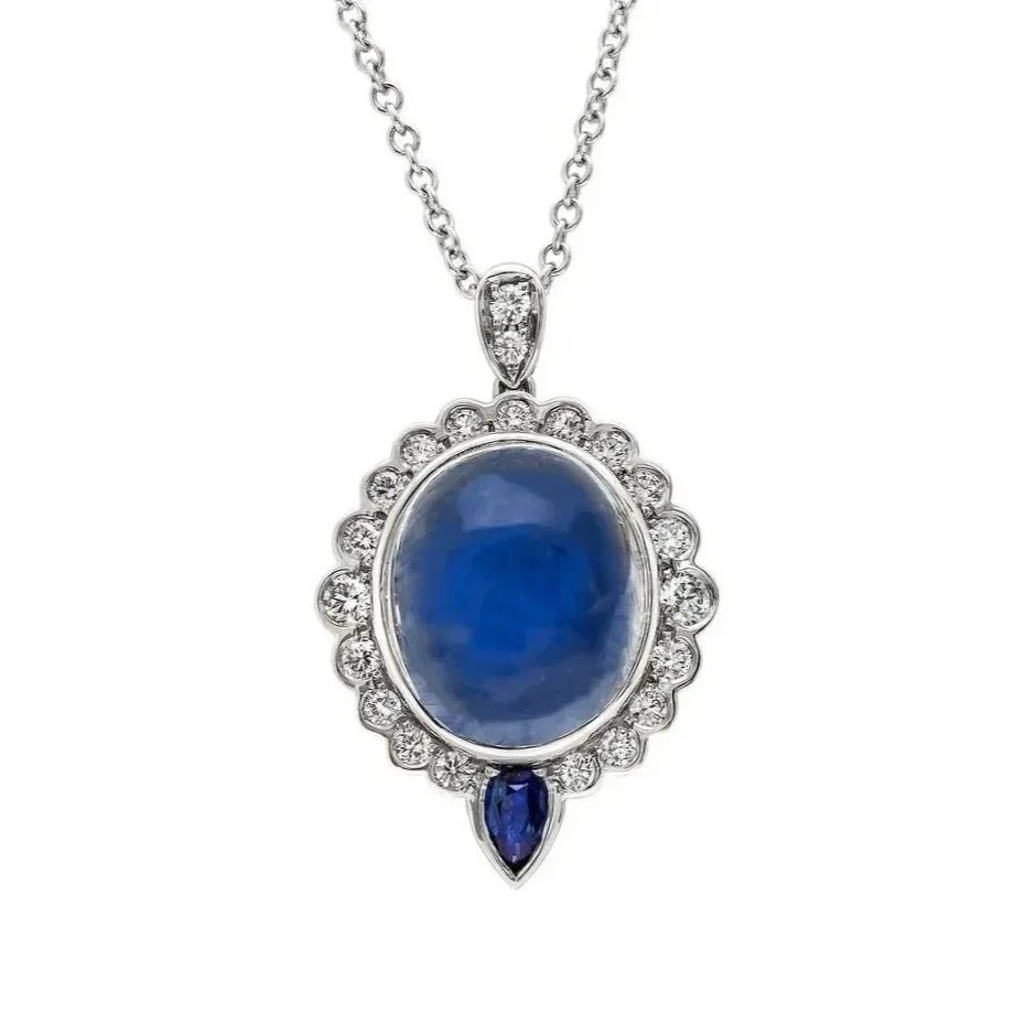 10.80 carat Oval Cabochon Moonstone Pendant. Surrounding the Moonstone are 0.56 carats of Round Brilliant Cut Diamonds and a .27 carat Pear Sapphire. A classic design with a vintage flair