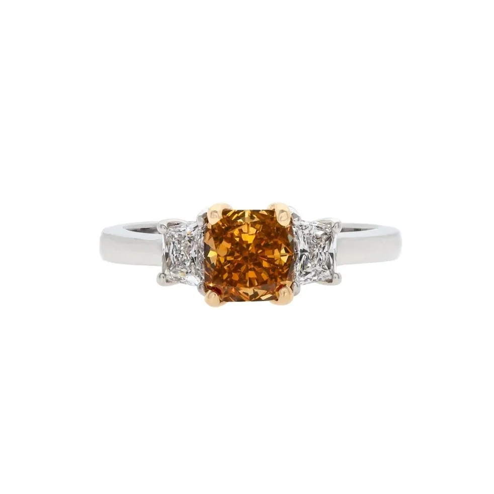 1.34 carat Radiant Cut Fancy Deep Brownish/Yellow Orange Diamond 3 stone Ring. 0.52 carats of Trapezoid Cut Diamonds surround the center stone. Set in 18k yellow gold and platinum.