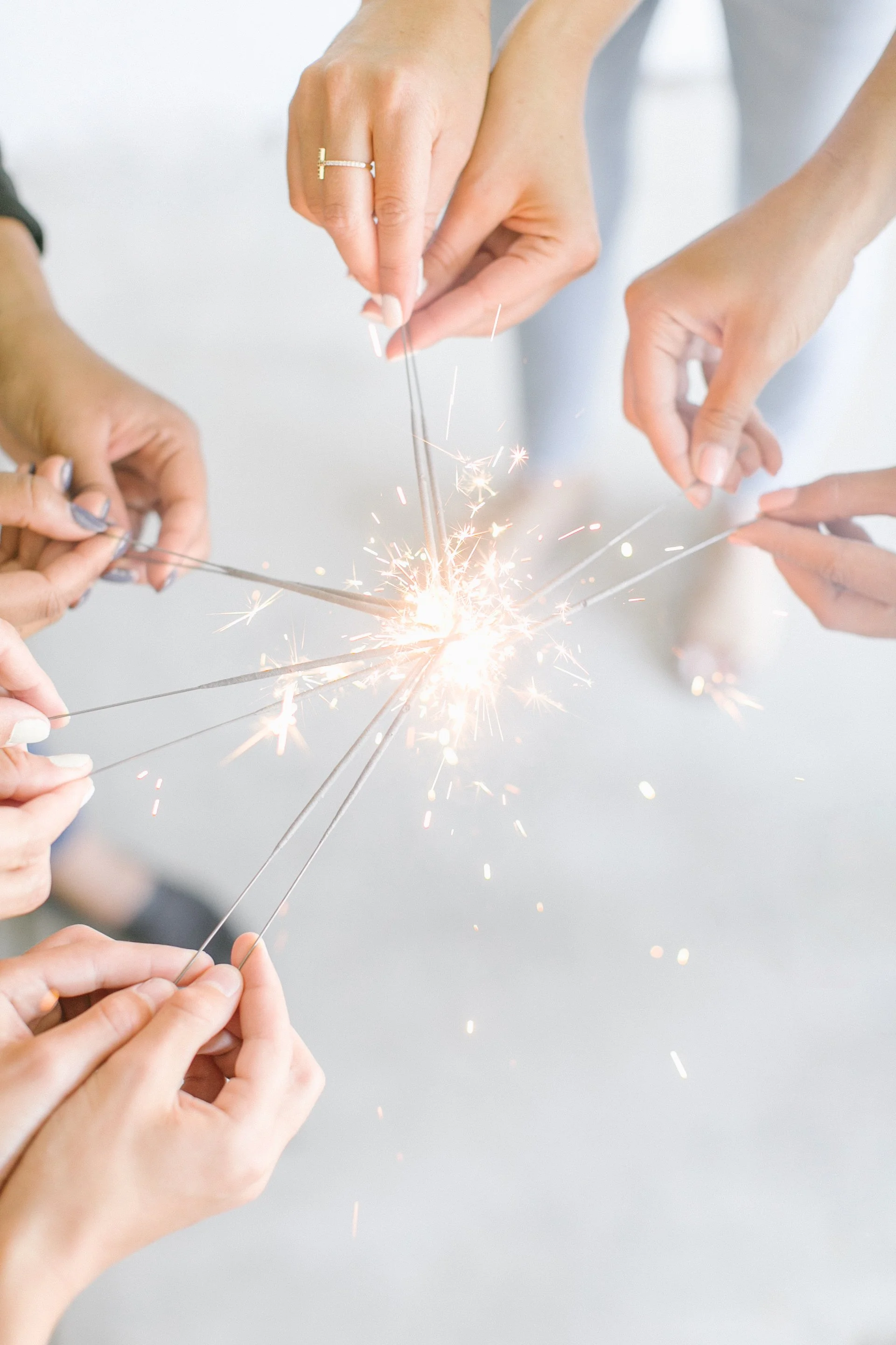Women’s hands holding sparklers together, representing connection, shared reflection, and community support.