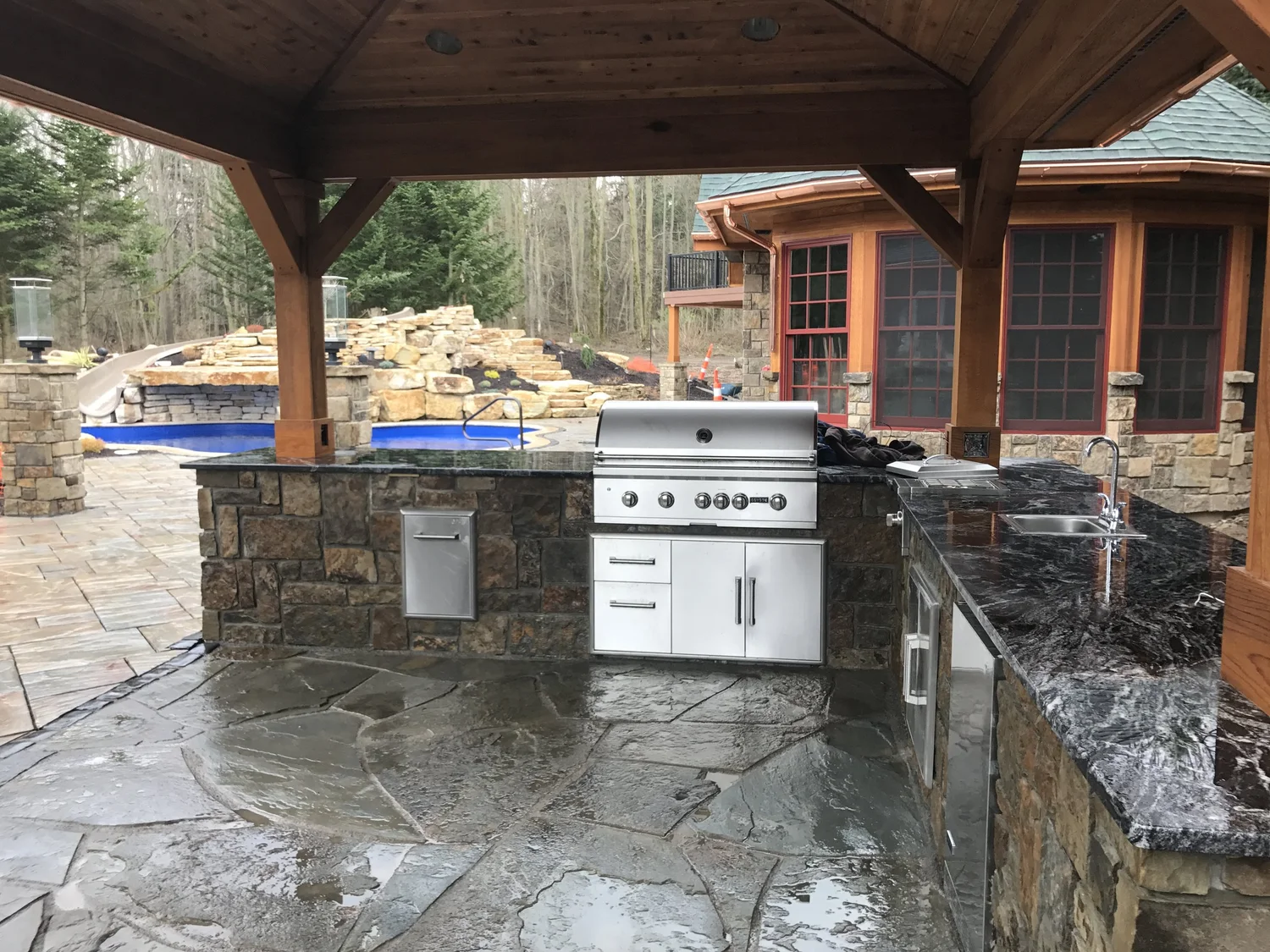 Outdoor living space Syracuse NY stone outdoor kitchen with grill under a timber pavilion